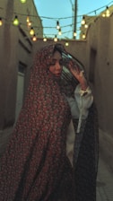 Woman in floral headscarf poses in alley.