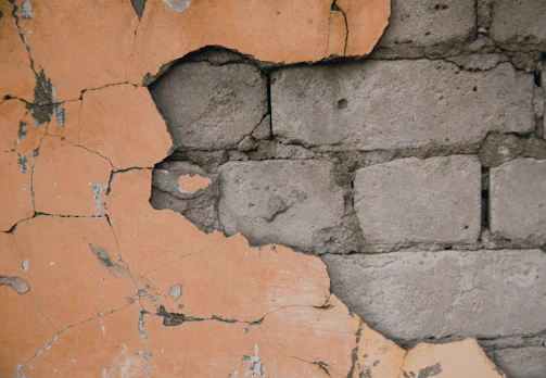 Cracked plaster reveals a weathered brick wall.