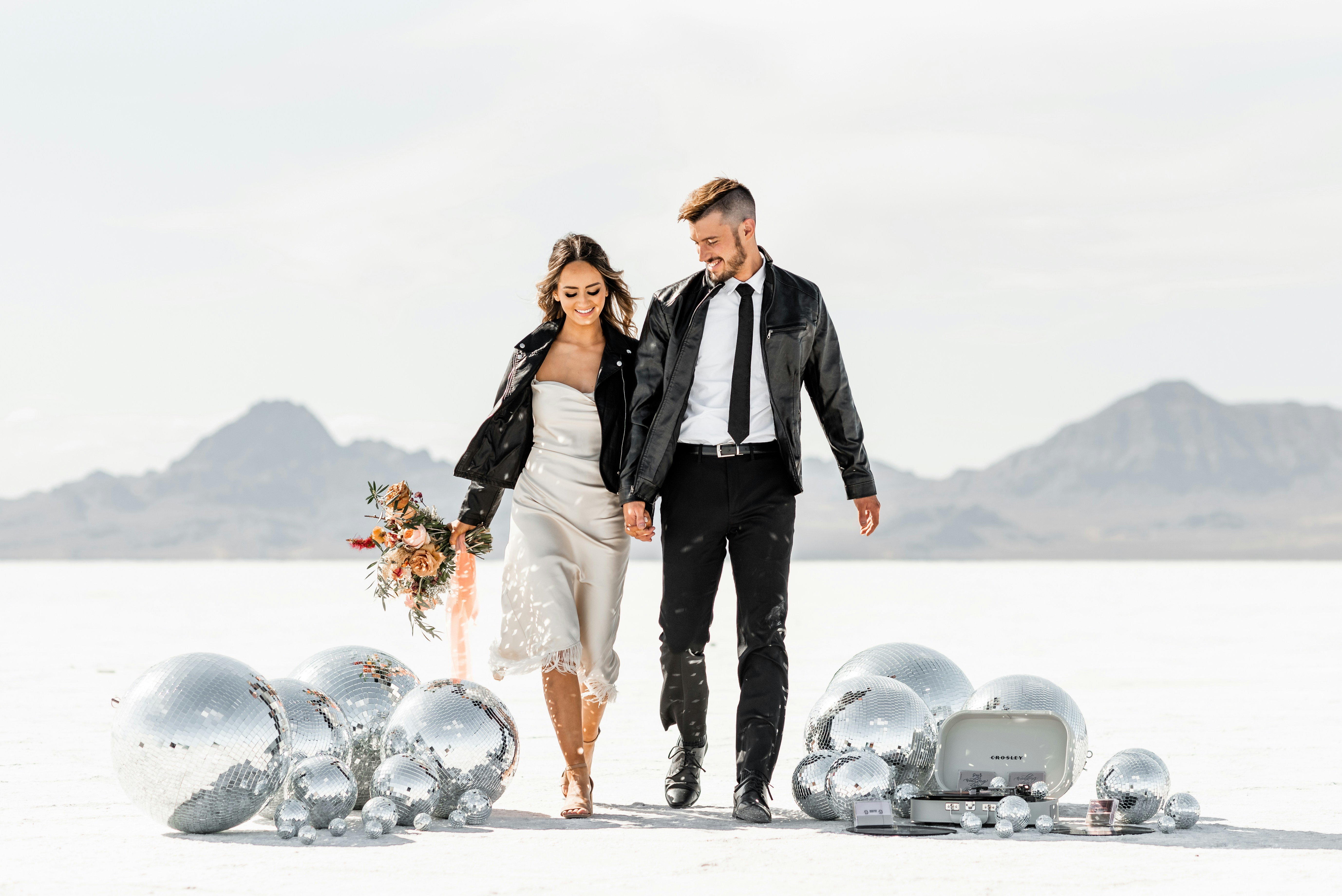 Newlyweds walk on a salt flat surrounded by disco balls.
