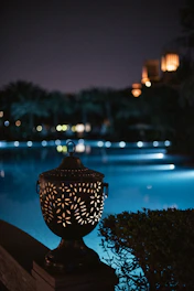 A decorative lantern glows by a pool at night.