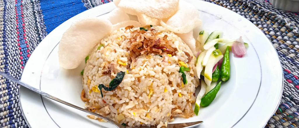 A plate of Indonesian nasi goreng with prawn crackers, cucumber, shallot and green chillies