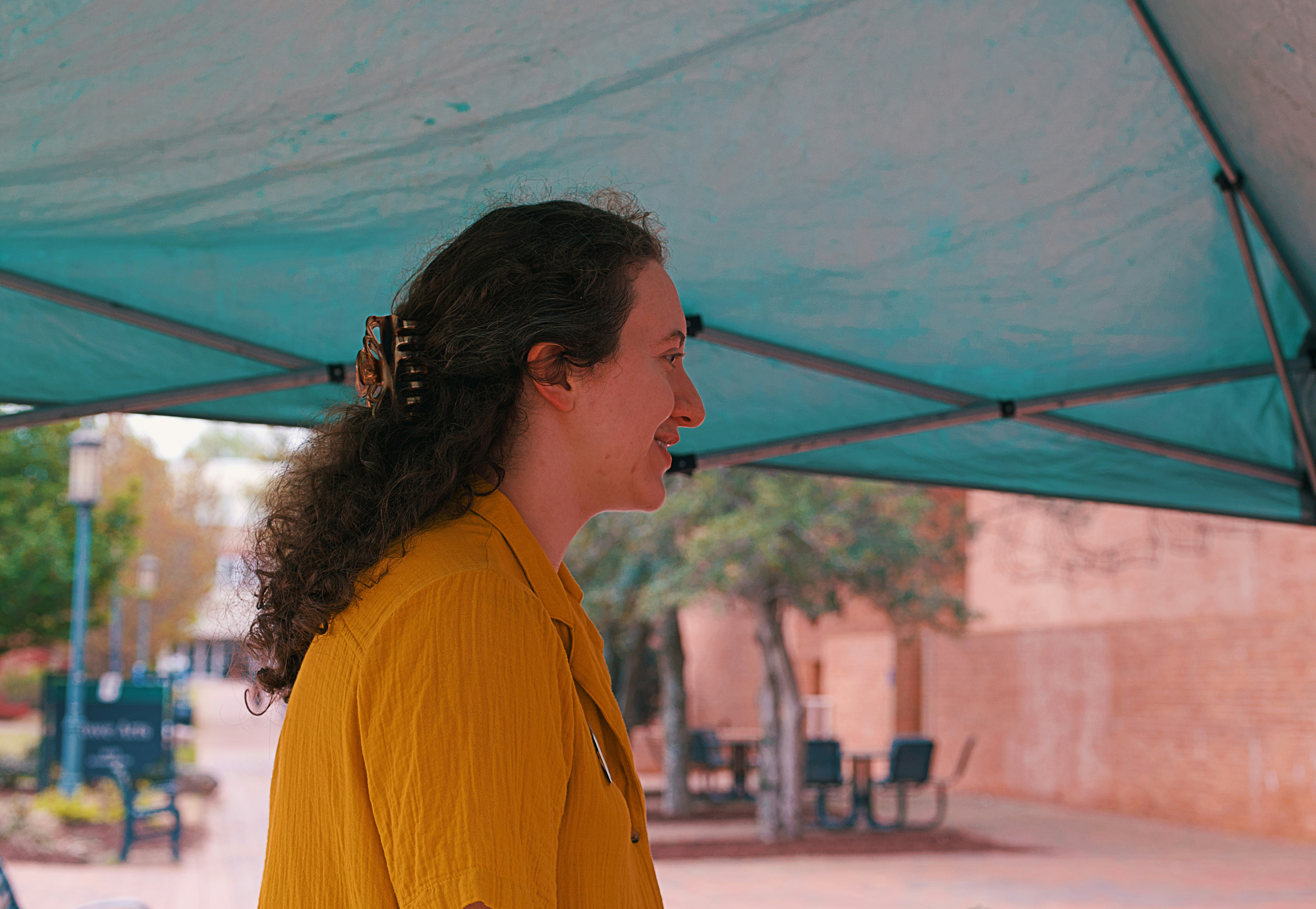 Woman smiles under a tent on a sunny day.