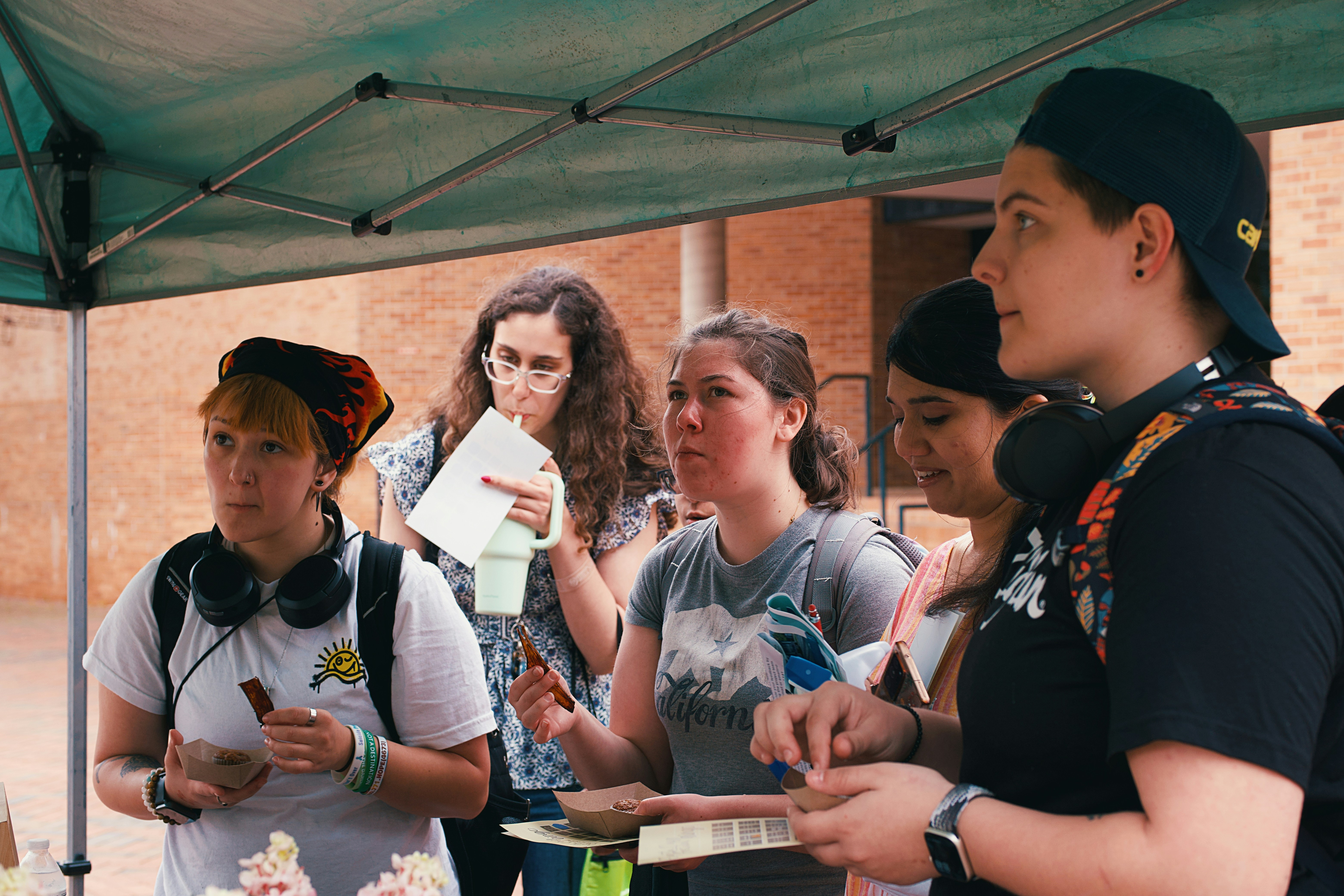 Group of women trying out banana muffins and banana peel bacon in cardboard containers.