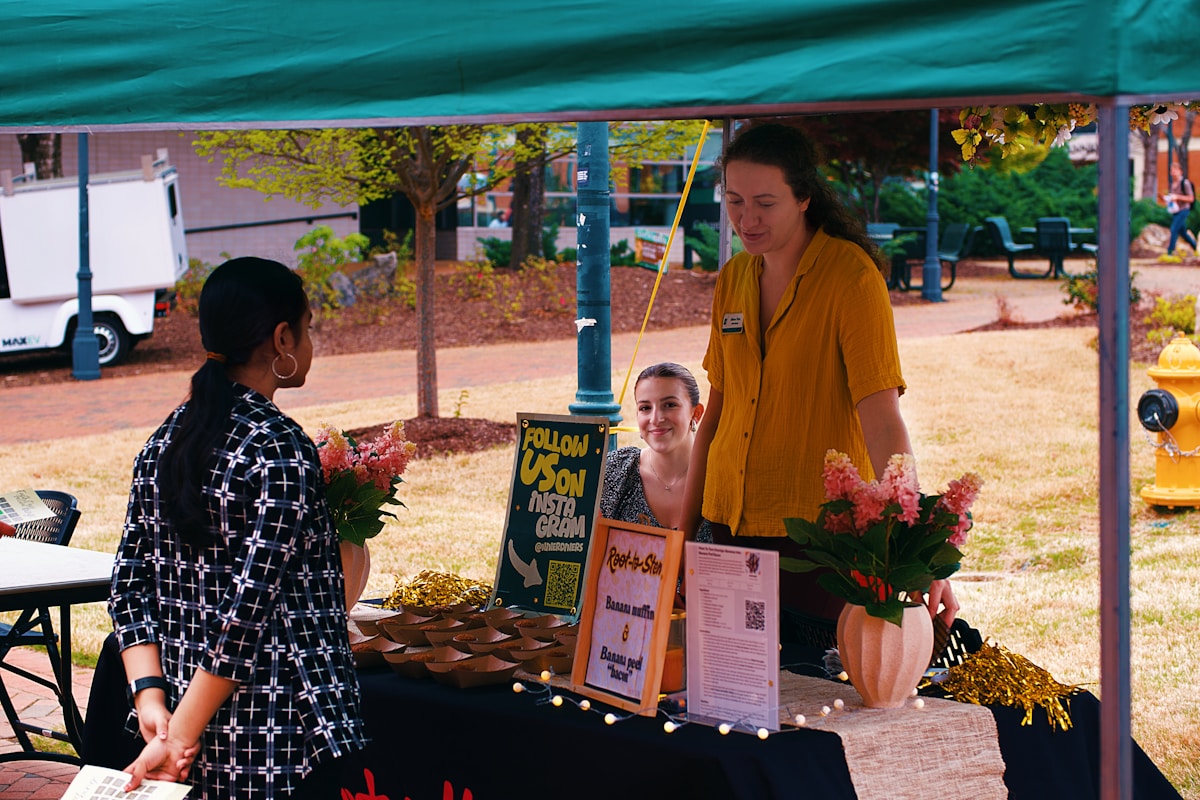A vendor at a market hands a gift to a smiling customer, illustrating volunteer appreciation event planning.