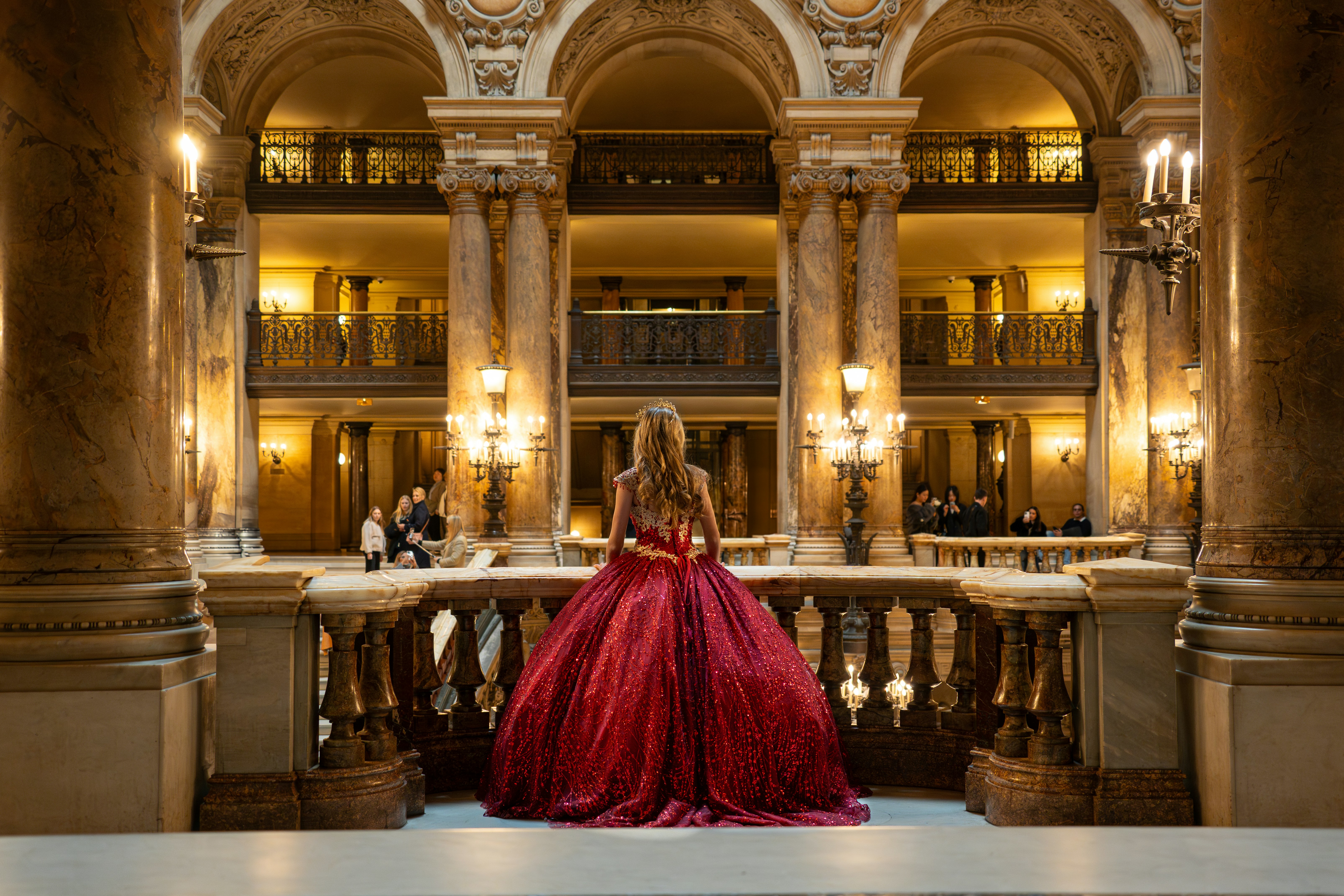 Woman in a red gown stands in a grand hall.