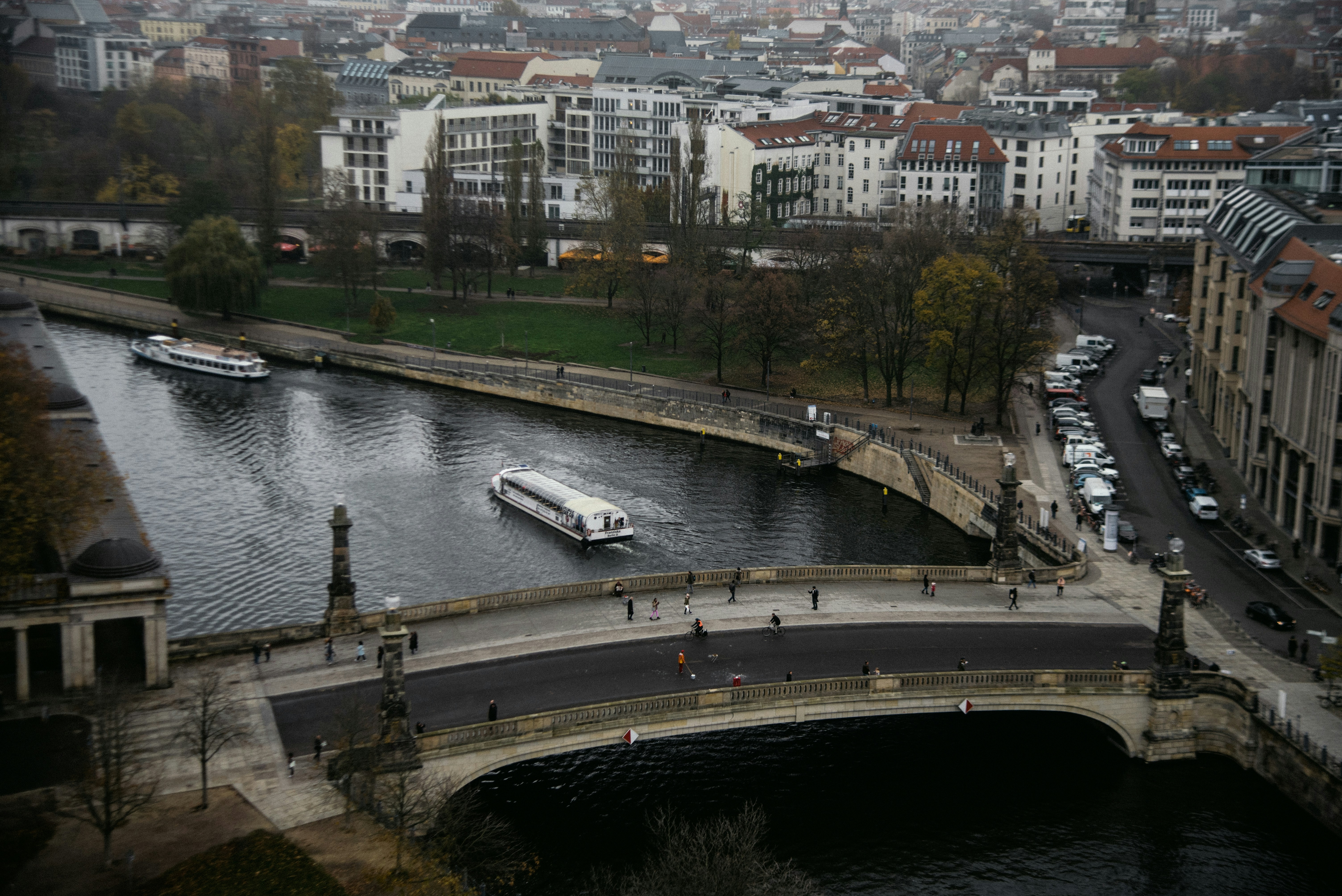 A cityscape shows a river and bridge with boats.