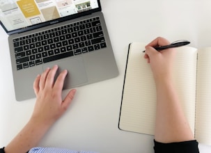 Person is working on a laptop and writing in a notebook.