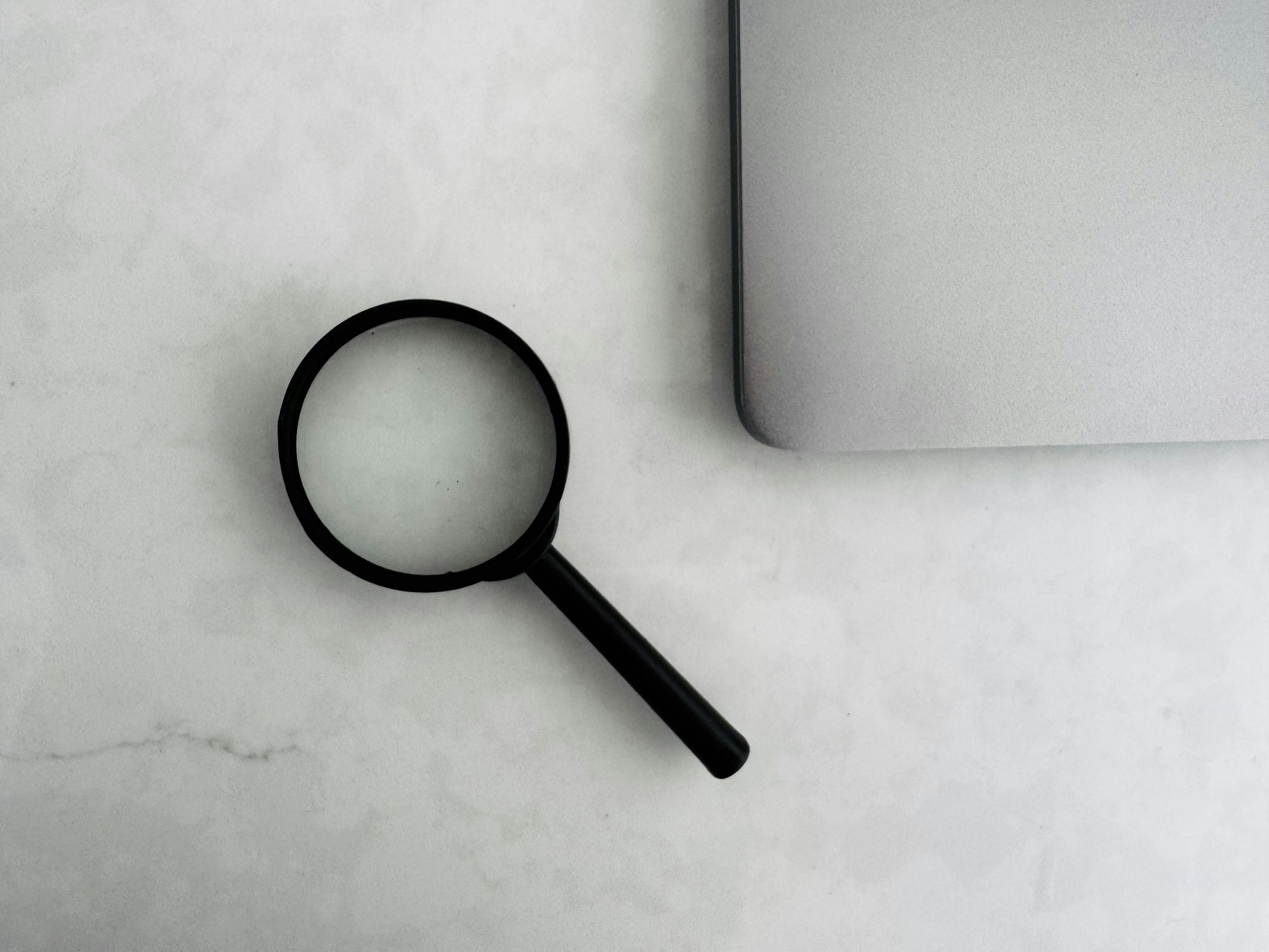 Magnifying glass beside the corner of a laptop on a marble surface