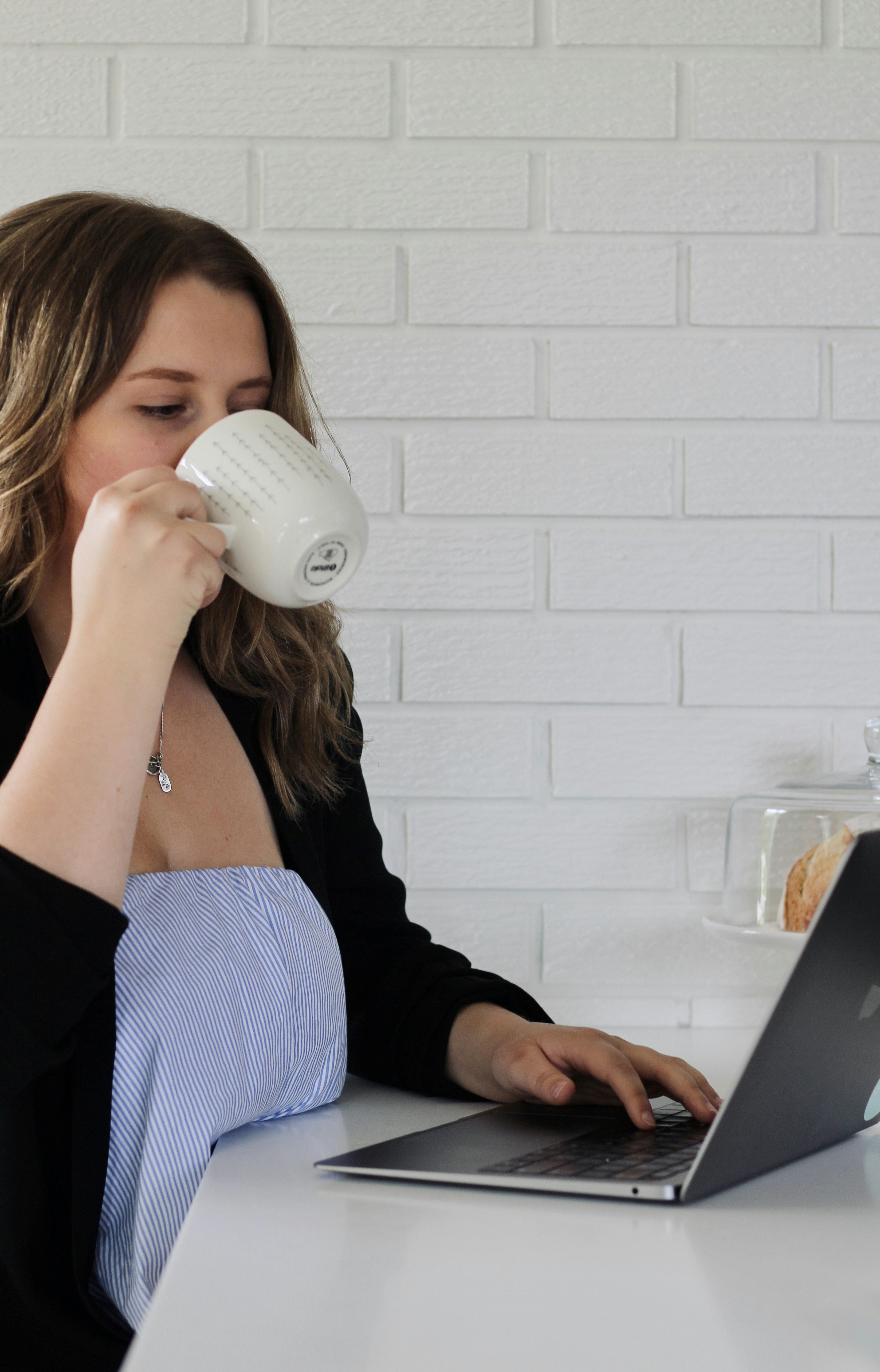 A woman drinks coffee while working on her laptop.