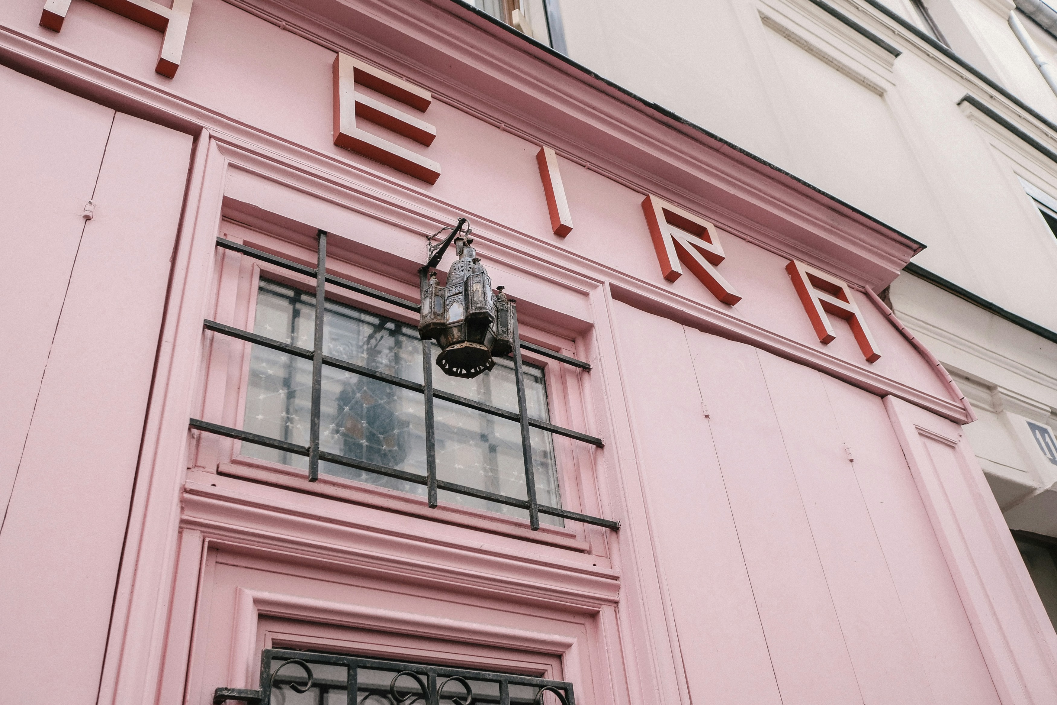 Pink building facade with a sign above a window.