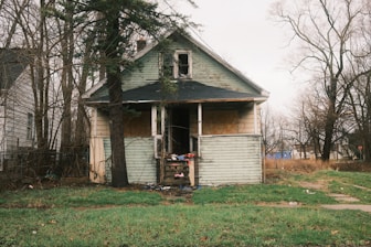 A dilapidated house sits in a neglected yard.