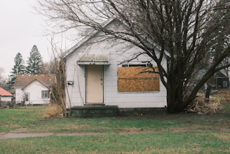 A boarded-up house sits in a yard.