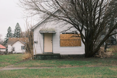 A boarded-up house sits in a yard.