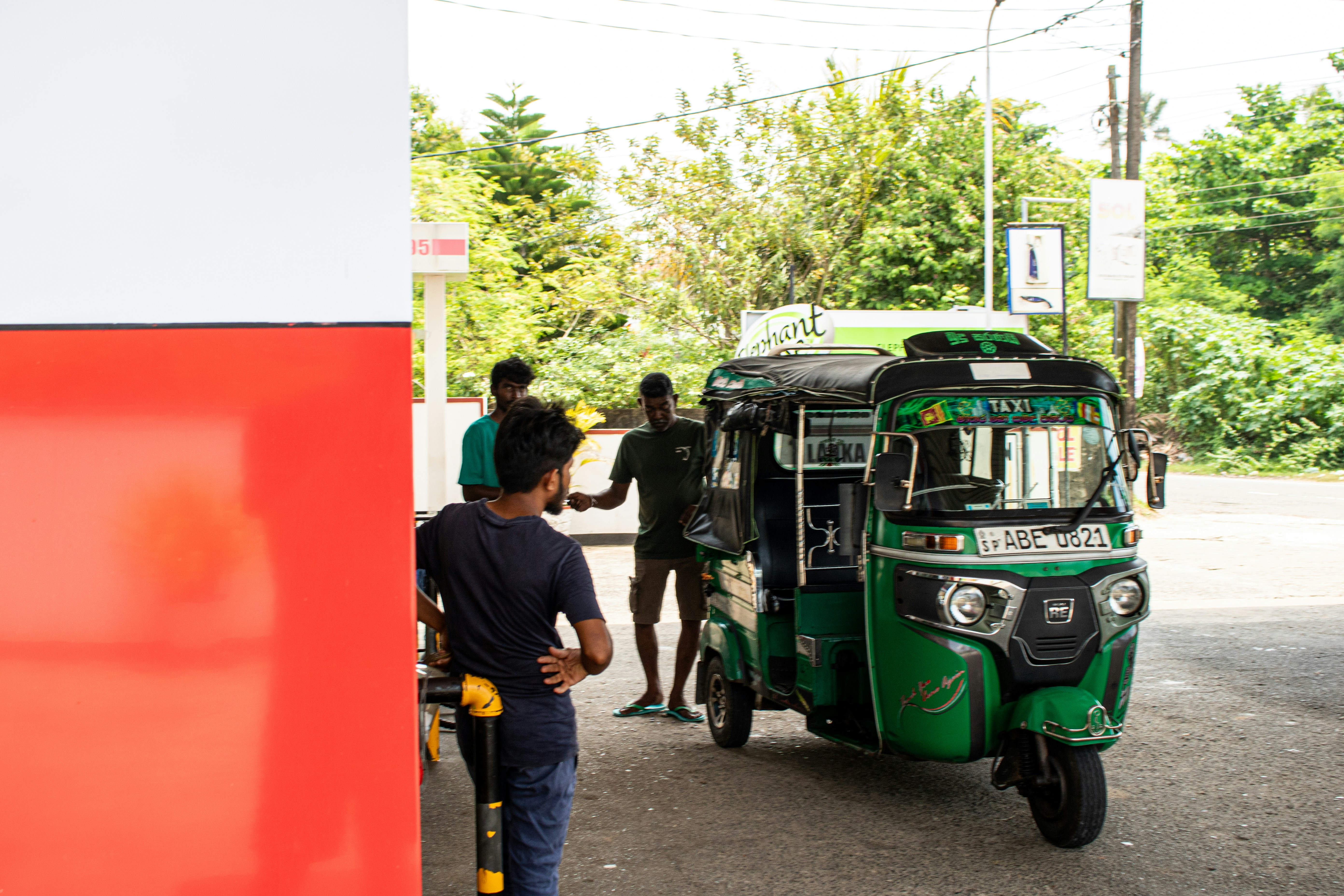 A green tuk-tuk is at a gas station.