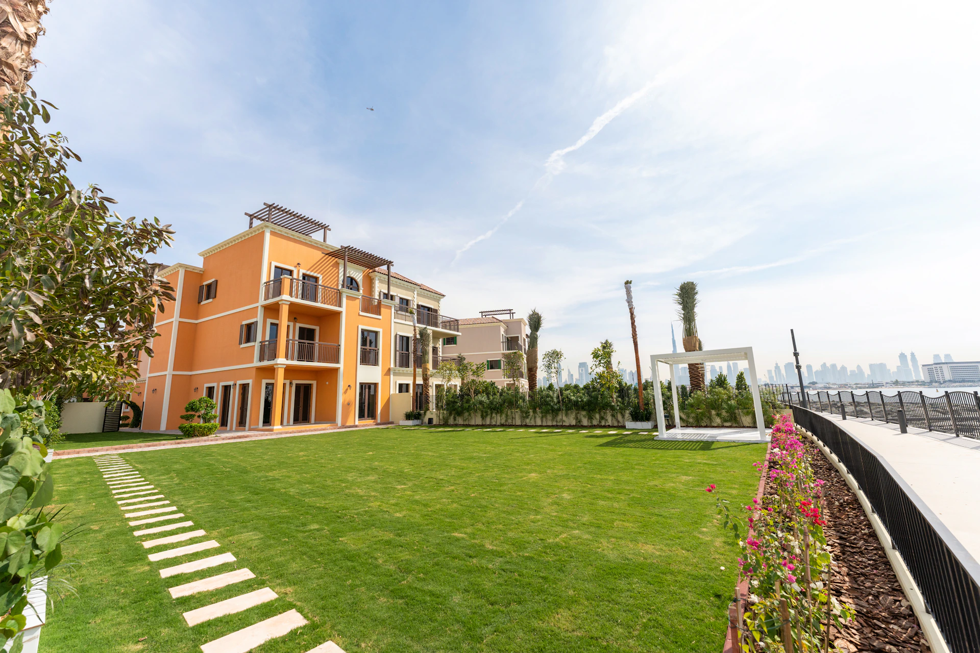Modern building with flowering vines beside a rectangular swimming pool and palm trees.