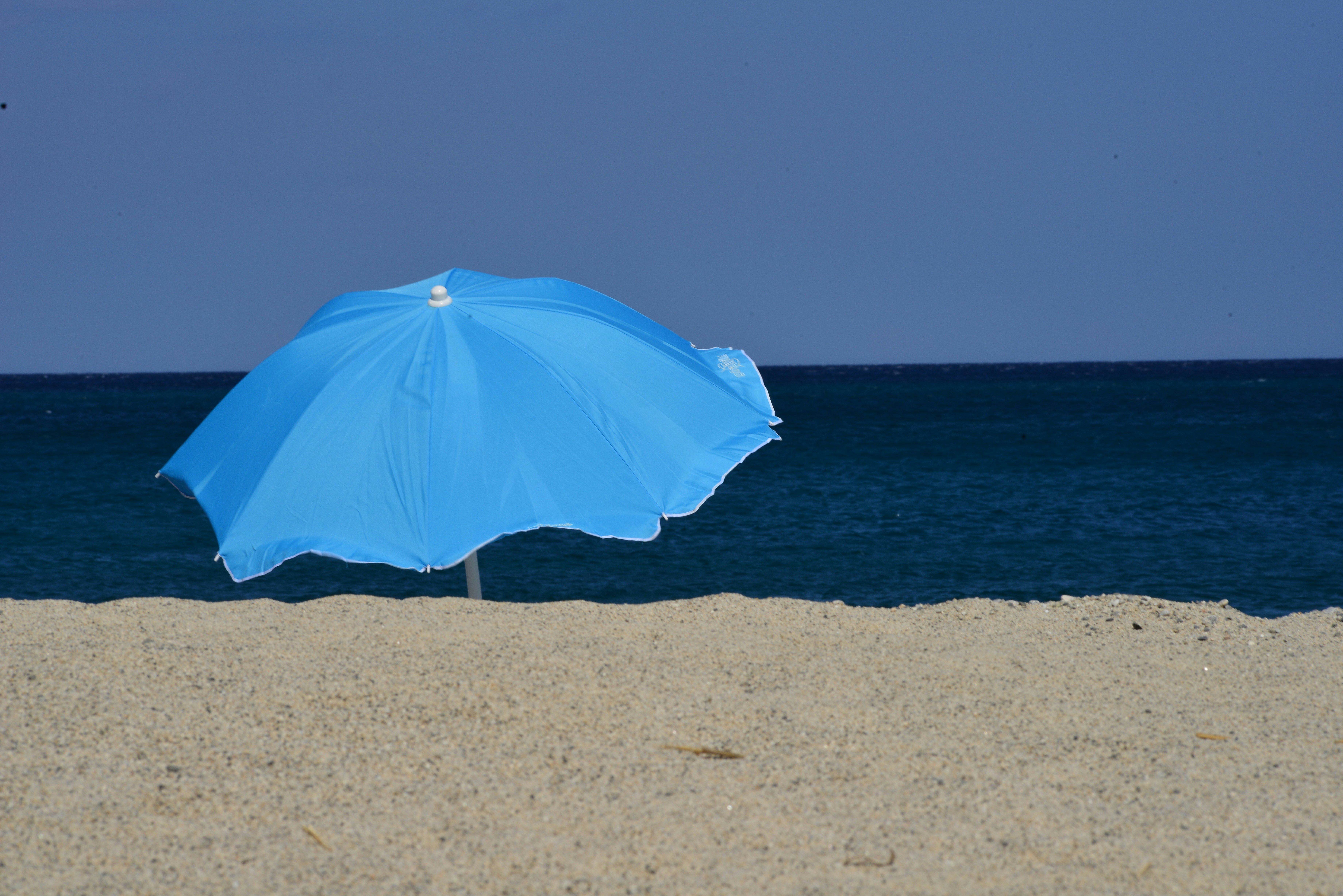A blue beach umbrella on a sandy beach.