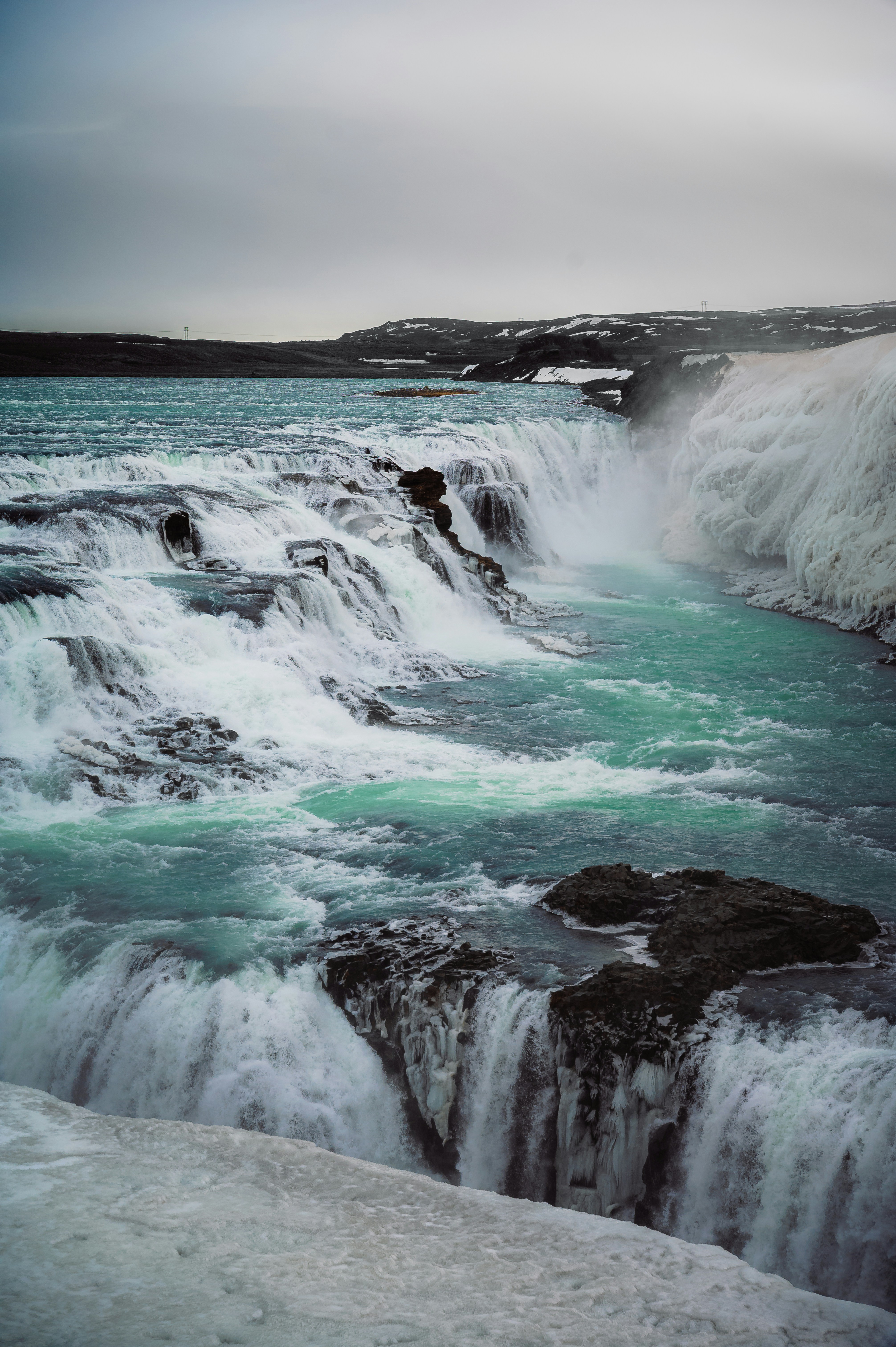 Turquoise waterfall cascades down rocky landscape.