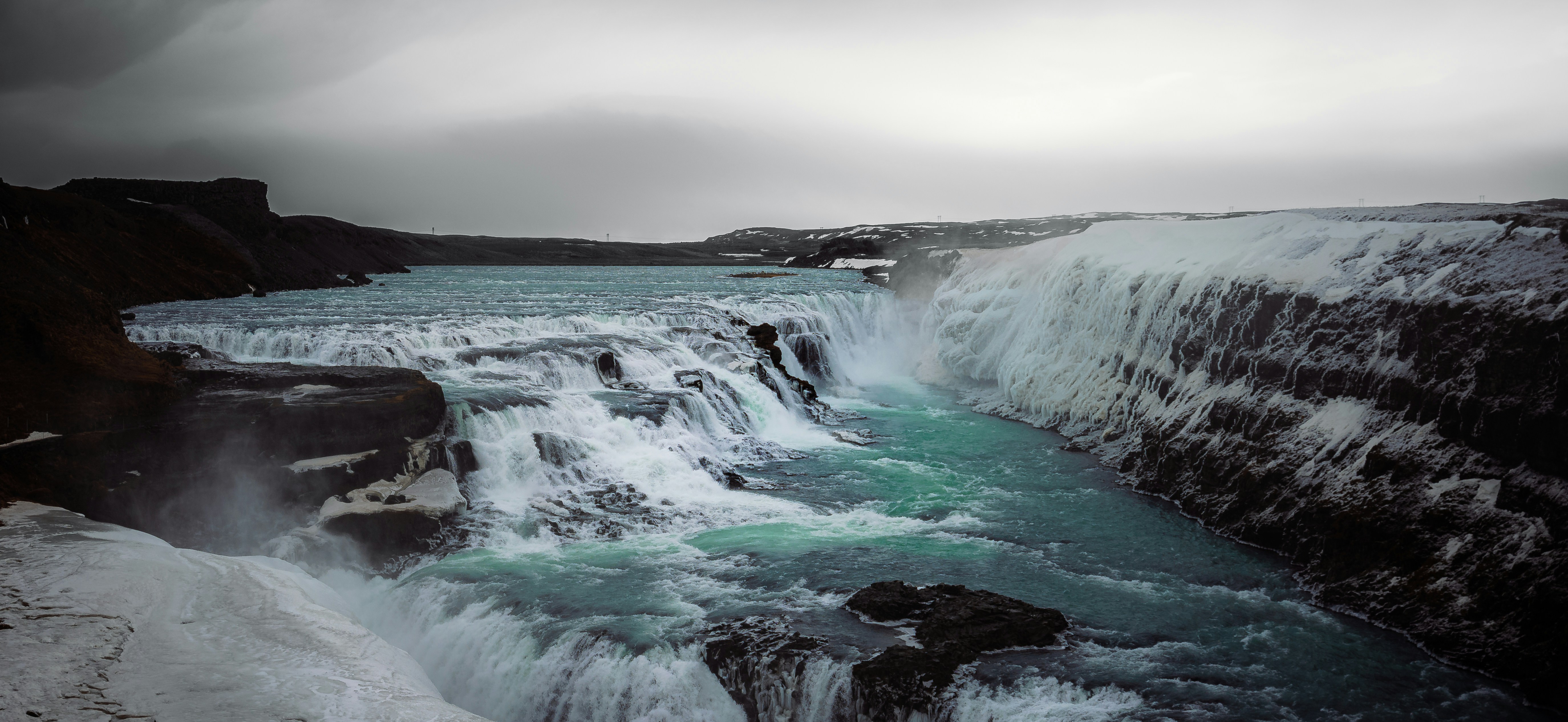 A powerful waterfall flows under a gray sky.