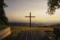 A cross stands on a hill overlooking the scenery.