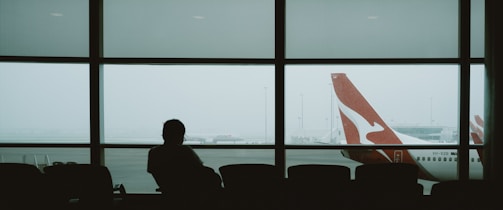 A person waits in an airport, watching a plane.