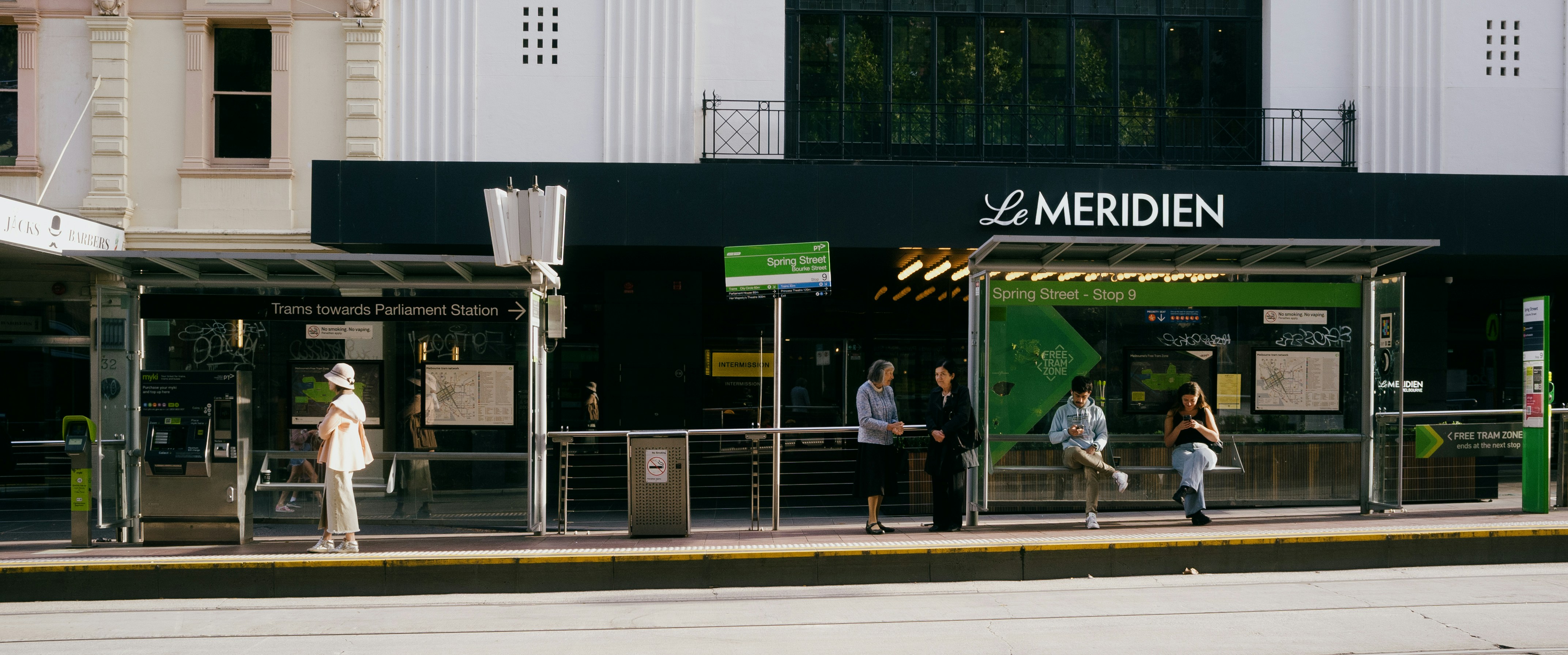 People wait at a bus stop near a hotel.