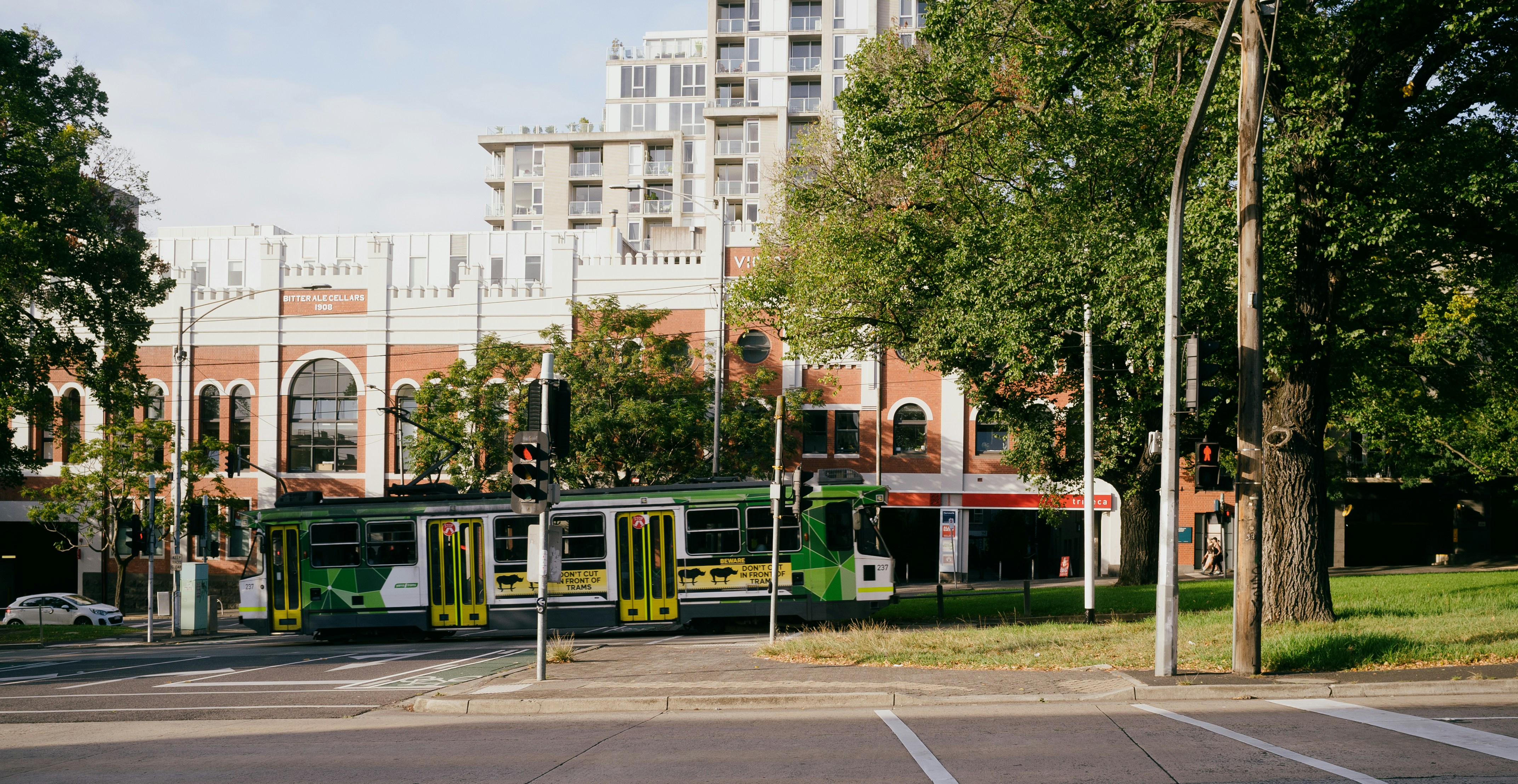 A green tram travels down the street.