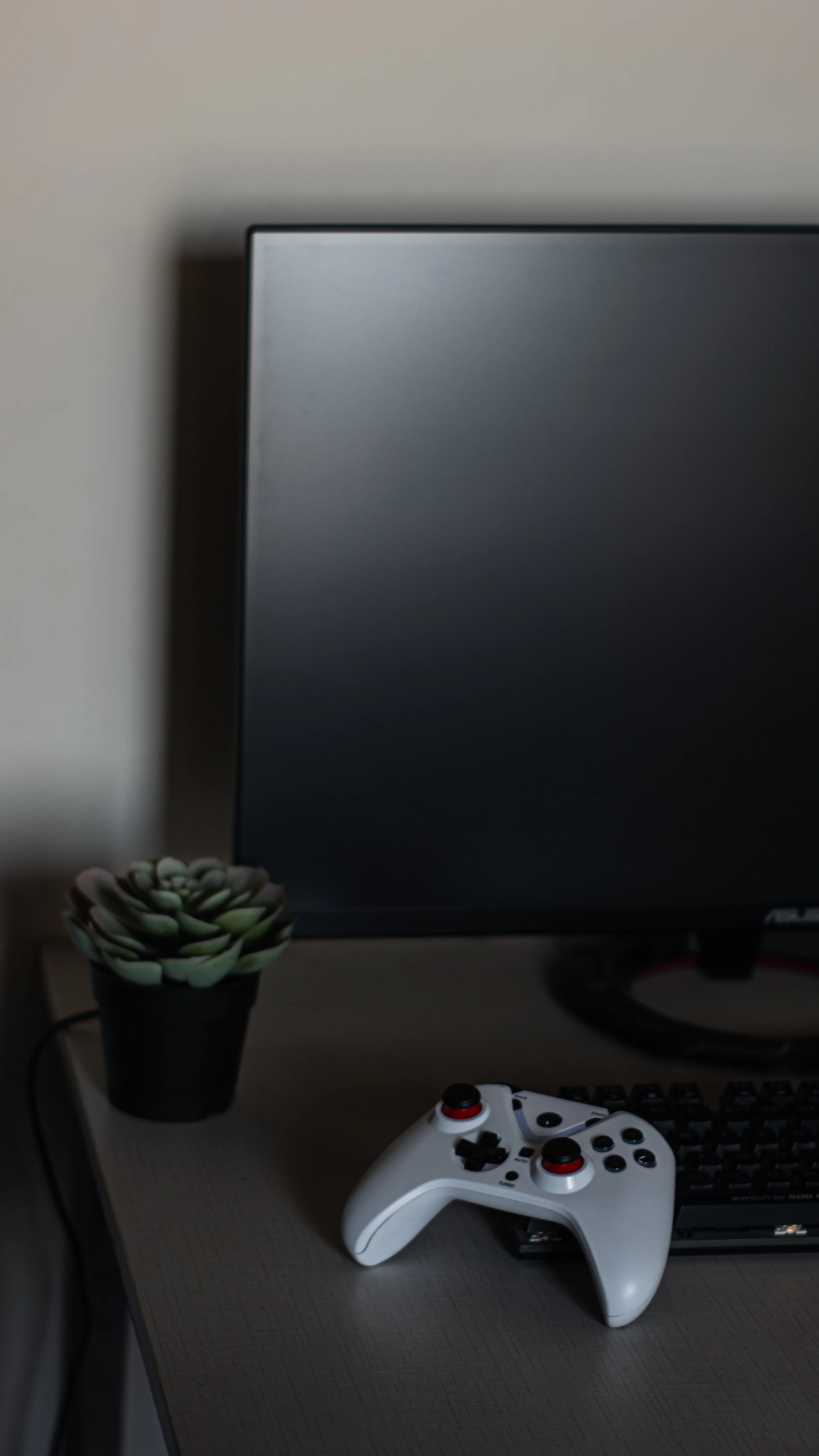 Gaming controller positioned in front of a monitor and keyboard in a dark gaming setup