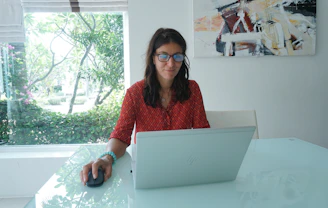 Woman works on laptop at a bright table.