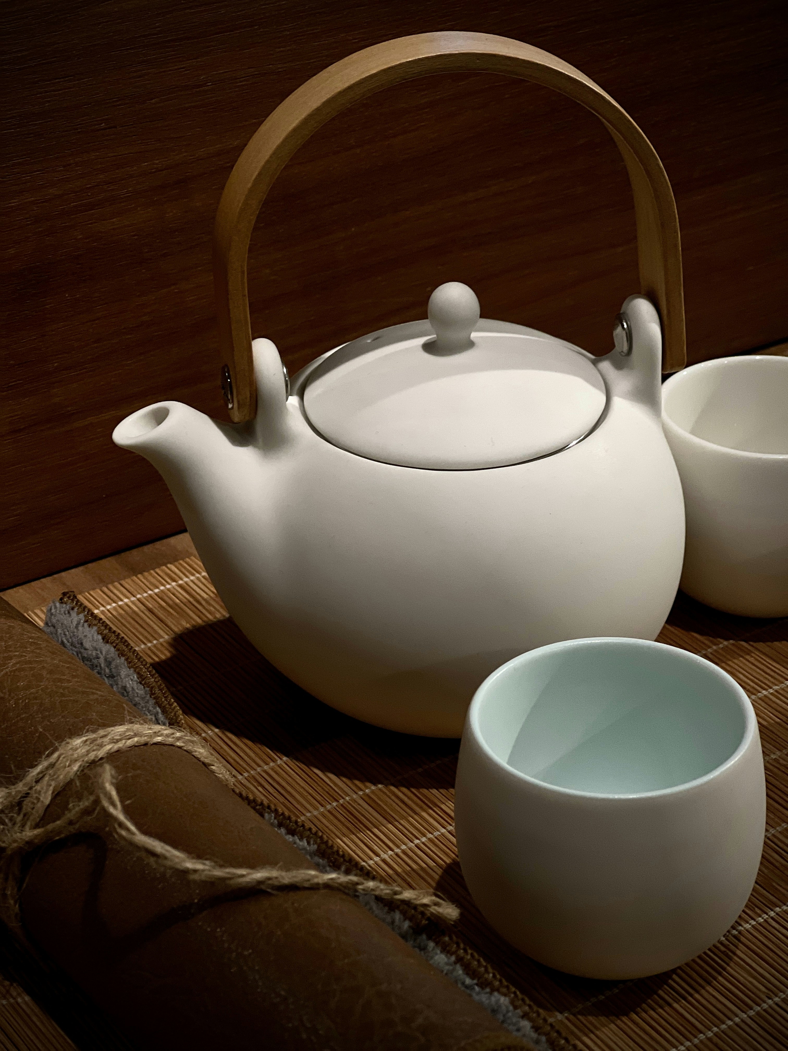 A white teapot and cups are ready for tea.