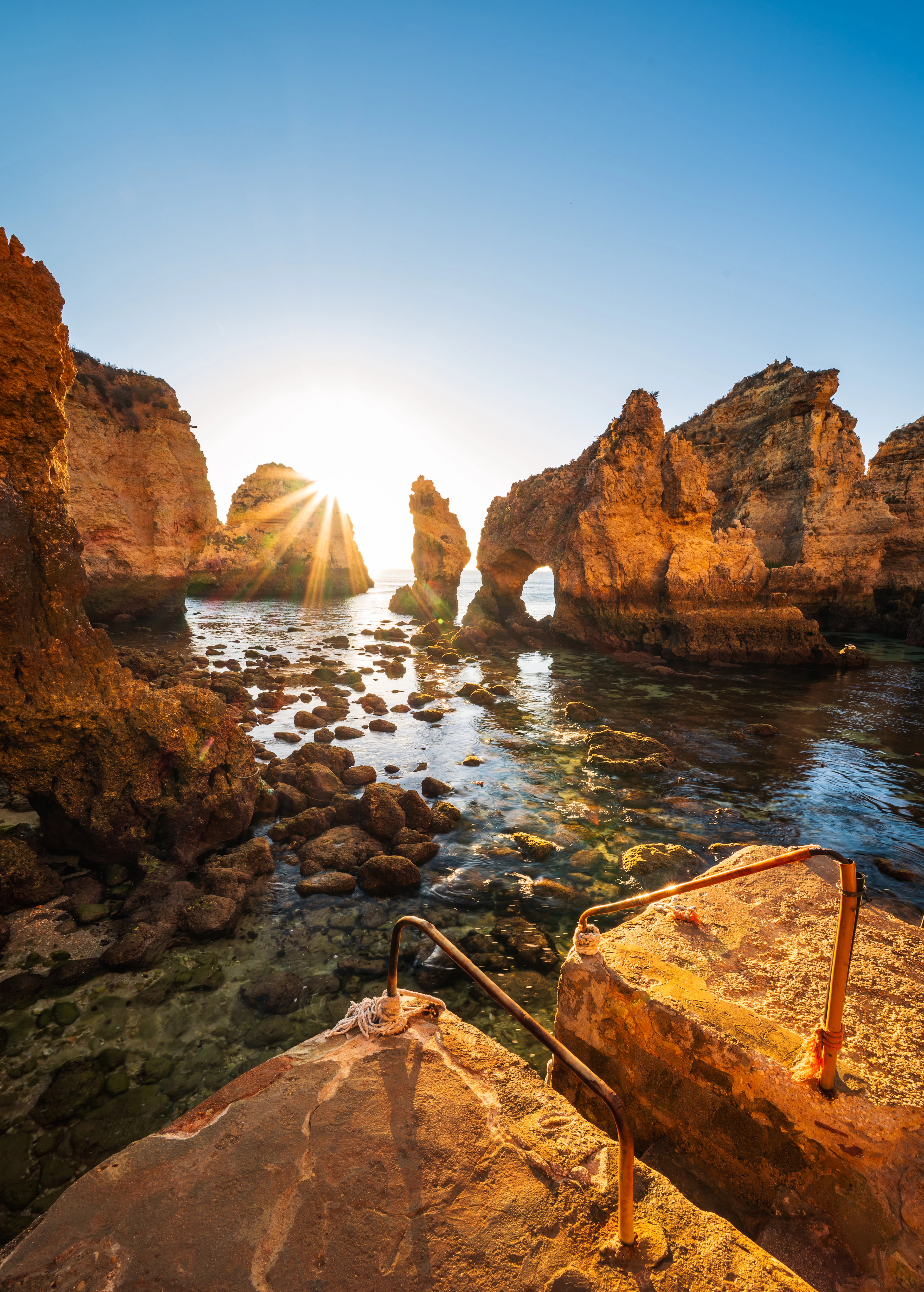 Sunrise bursts through a rock arch at Ponta da Piedade, lighting the cliffs gold.