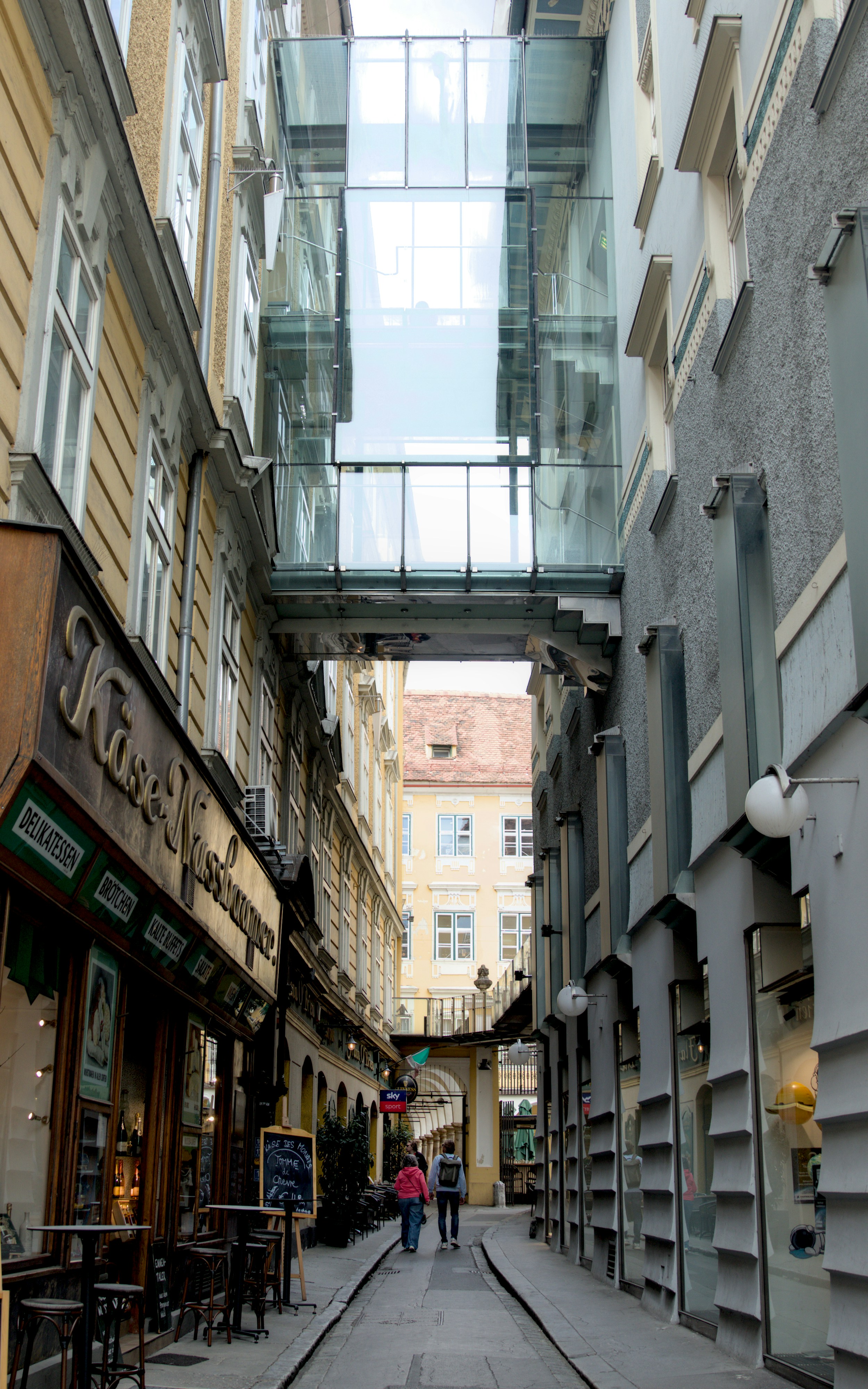 People walk down a narrow street with glass walkways.