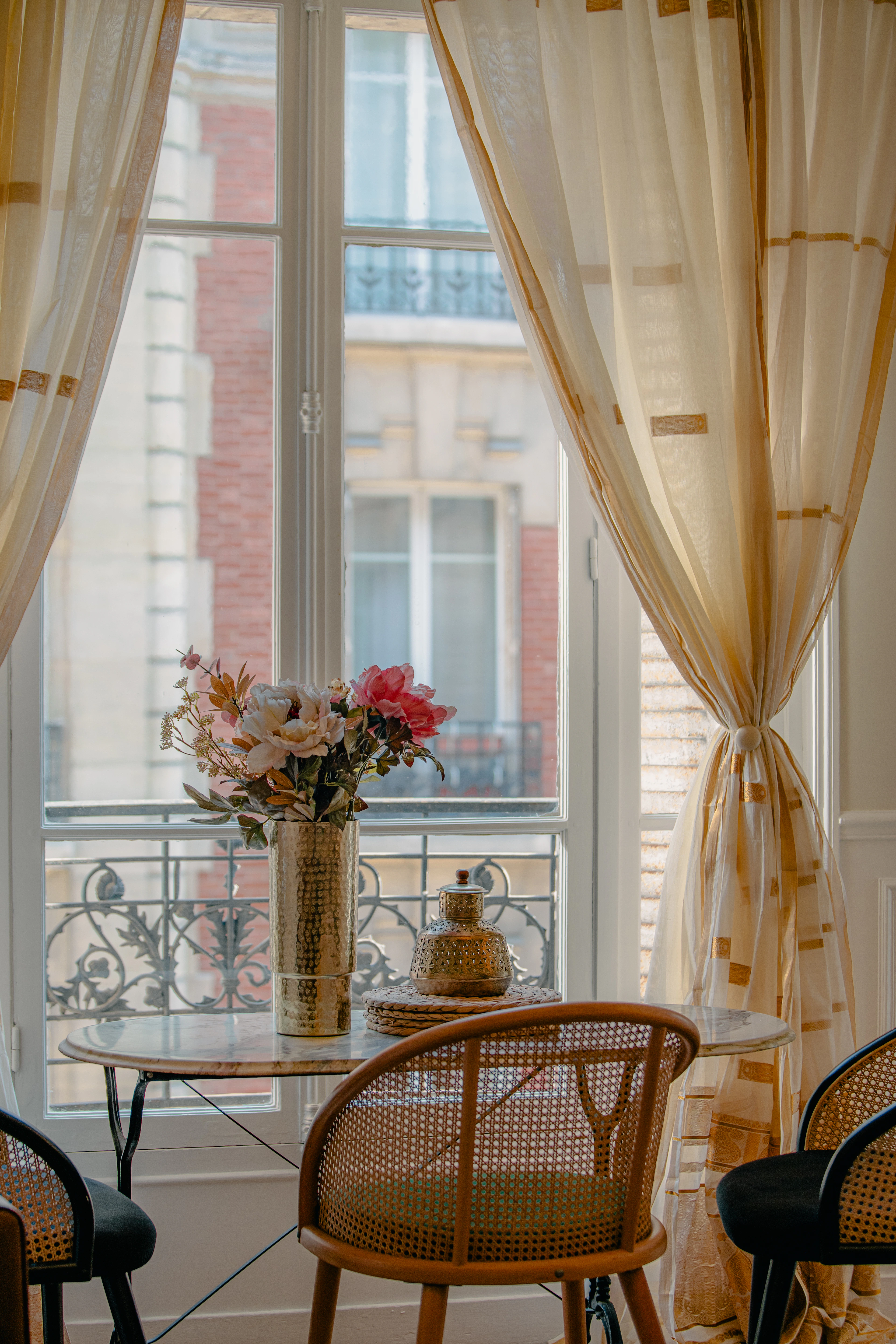 A furnished Parisian apartment: a small dining table set by open balcony doors, flowers on the table