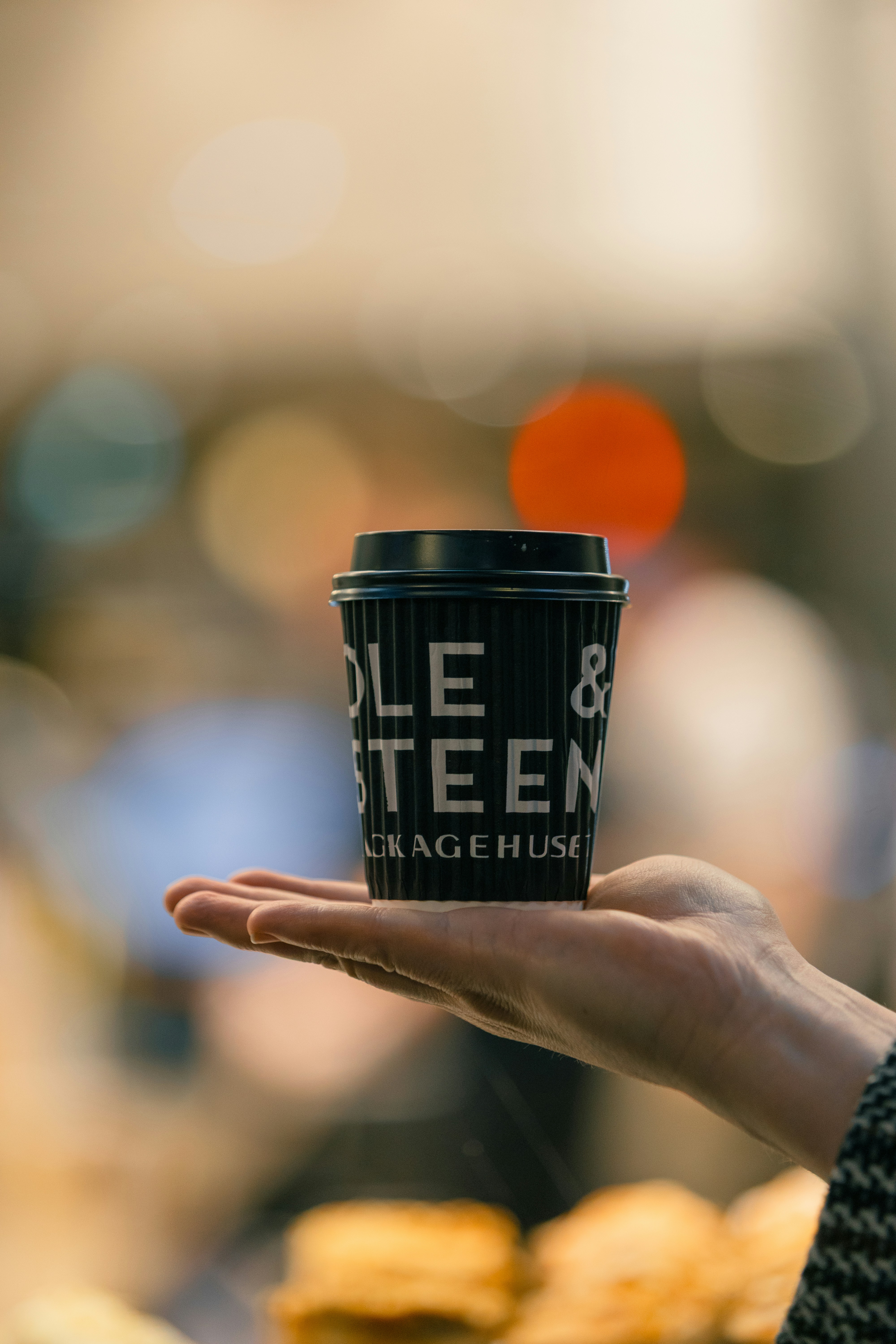 A hand holds a coffee cup against a blurred background