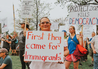 Protesters hold signs about immigrants and democracy.