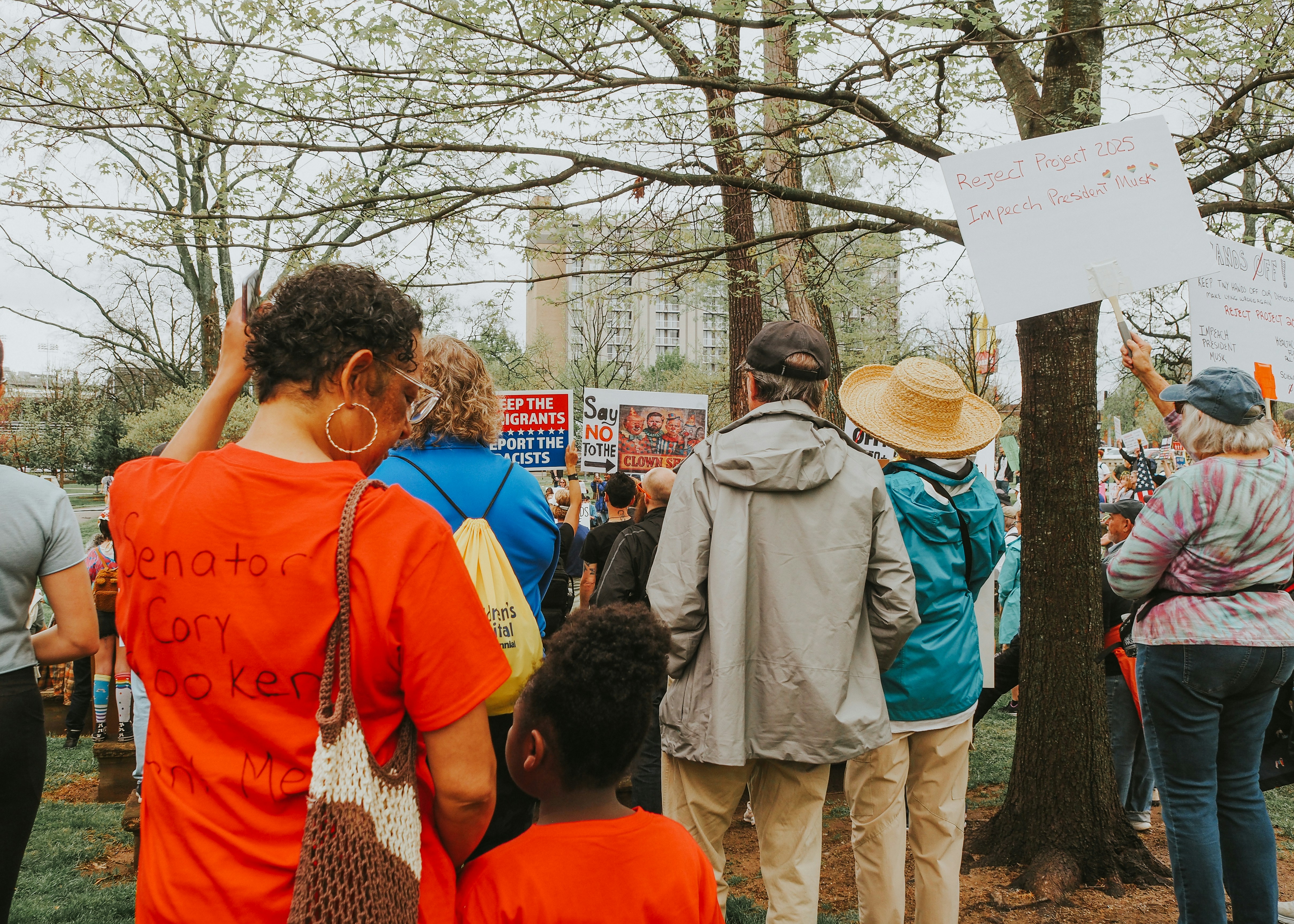People gather in a park holding signs.