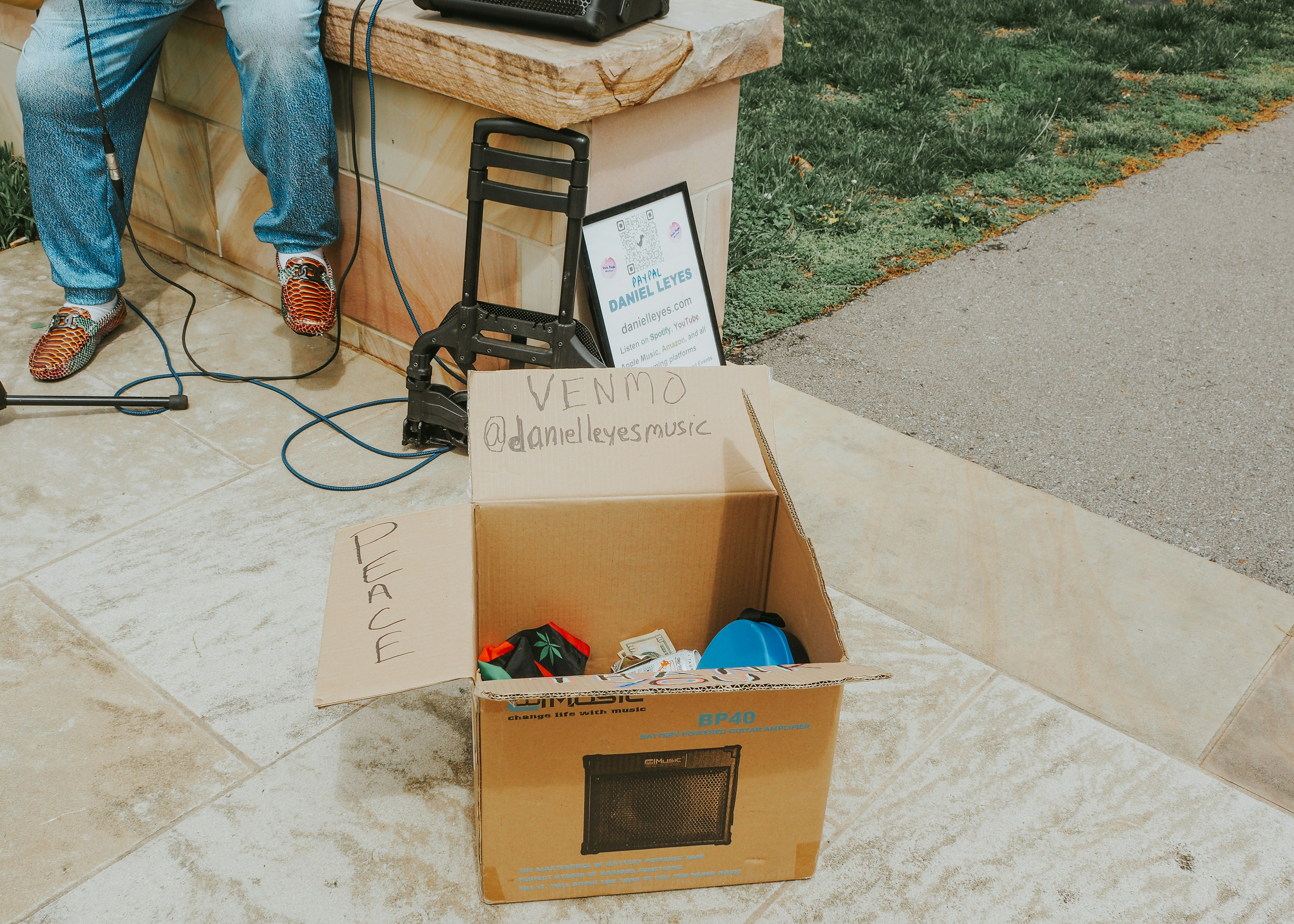 A donation box sits near a street performer.