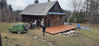 People are working on a wooden deck near a cabin.