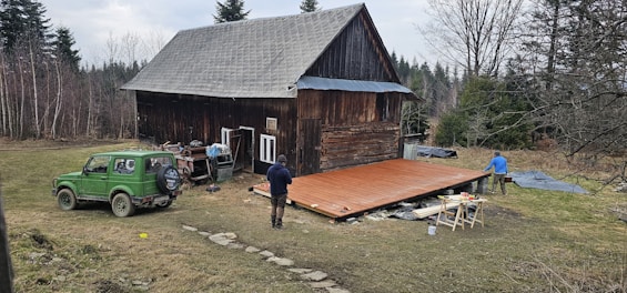 People are working on a wooden deck near a cabin.