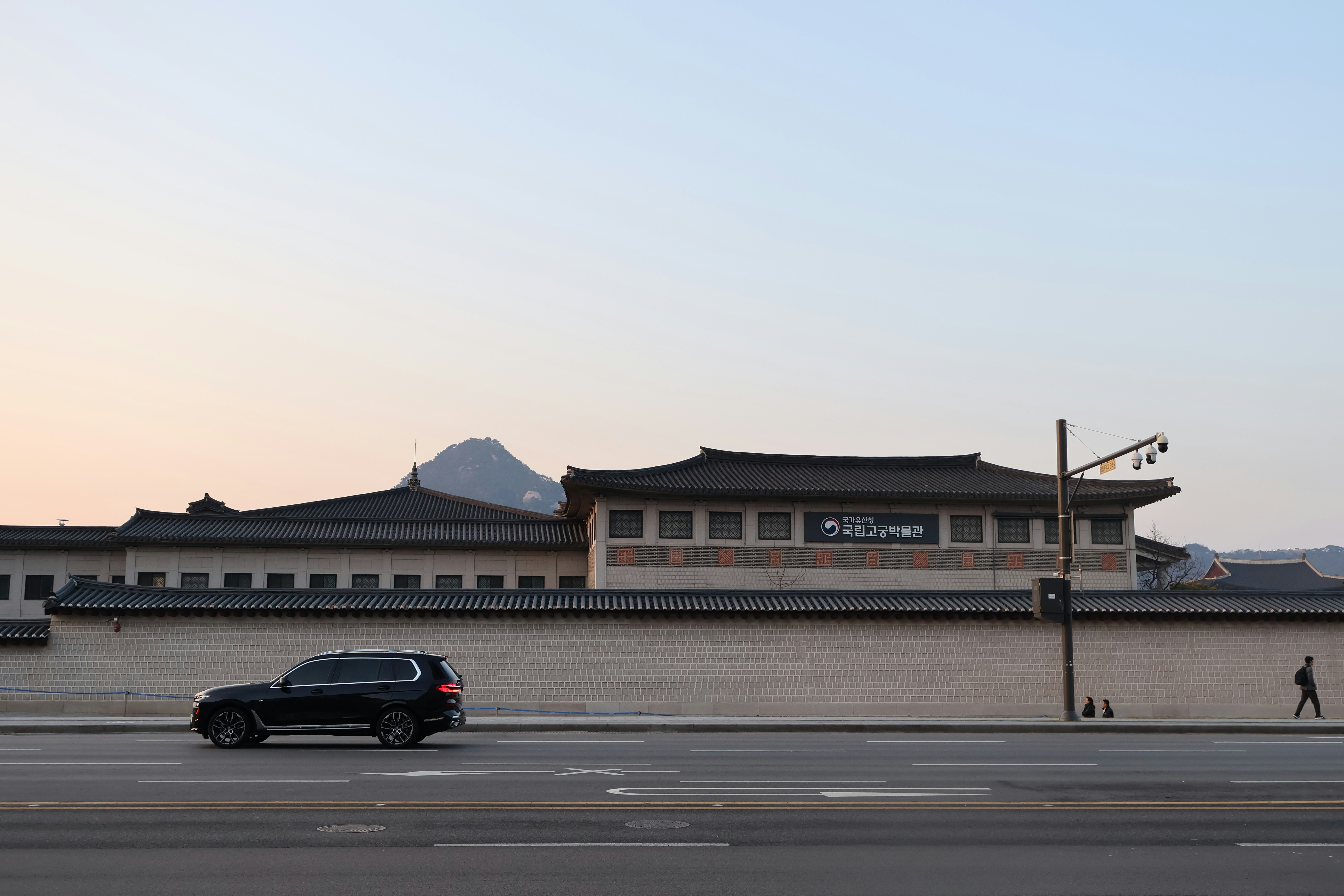 A car drives past a building and mountain.