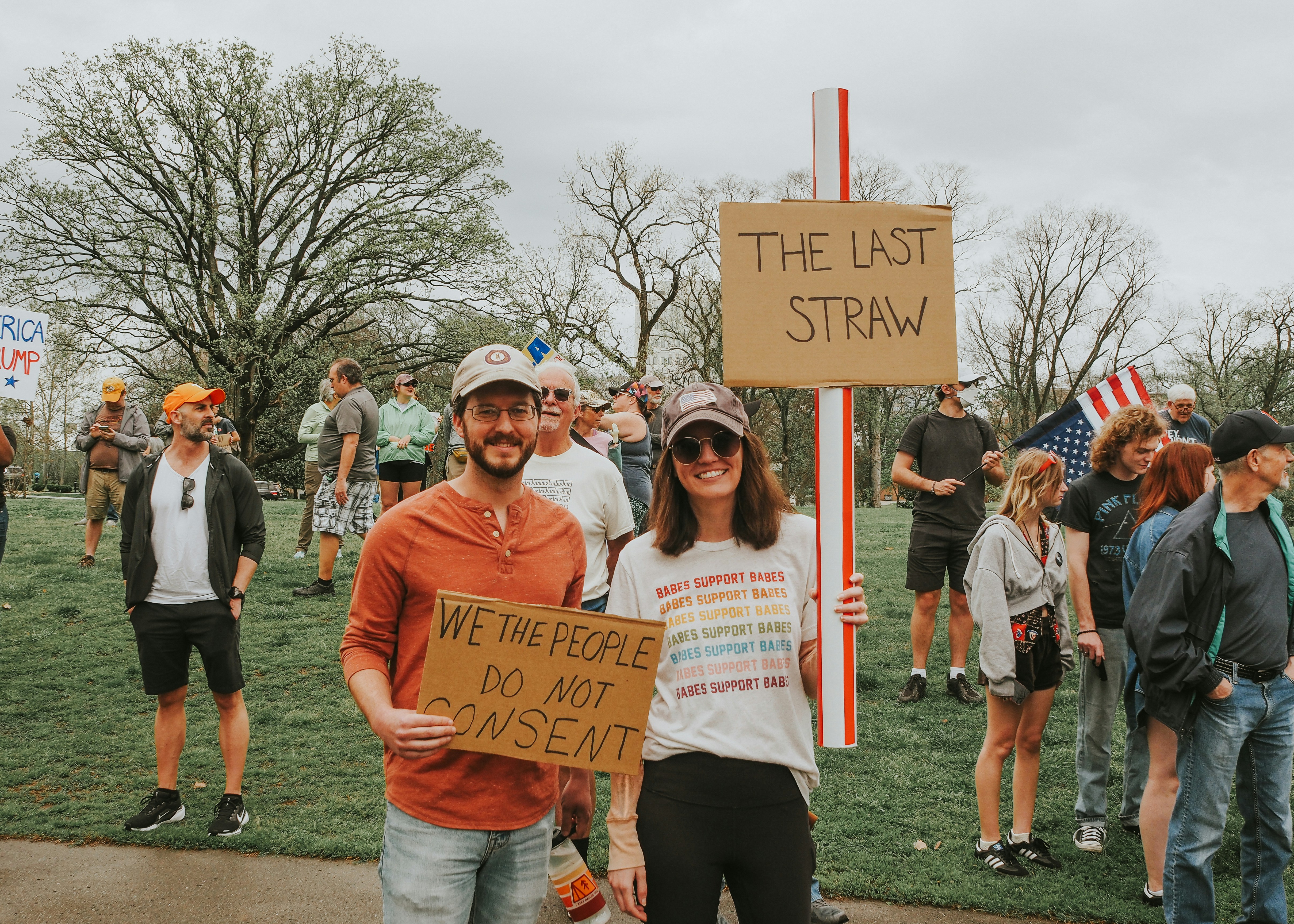 People protest with signs at an outdoor rally.