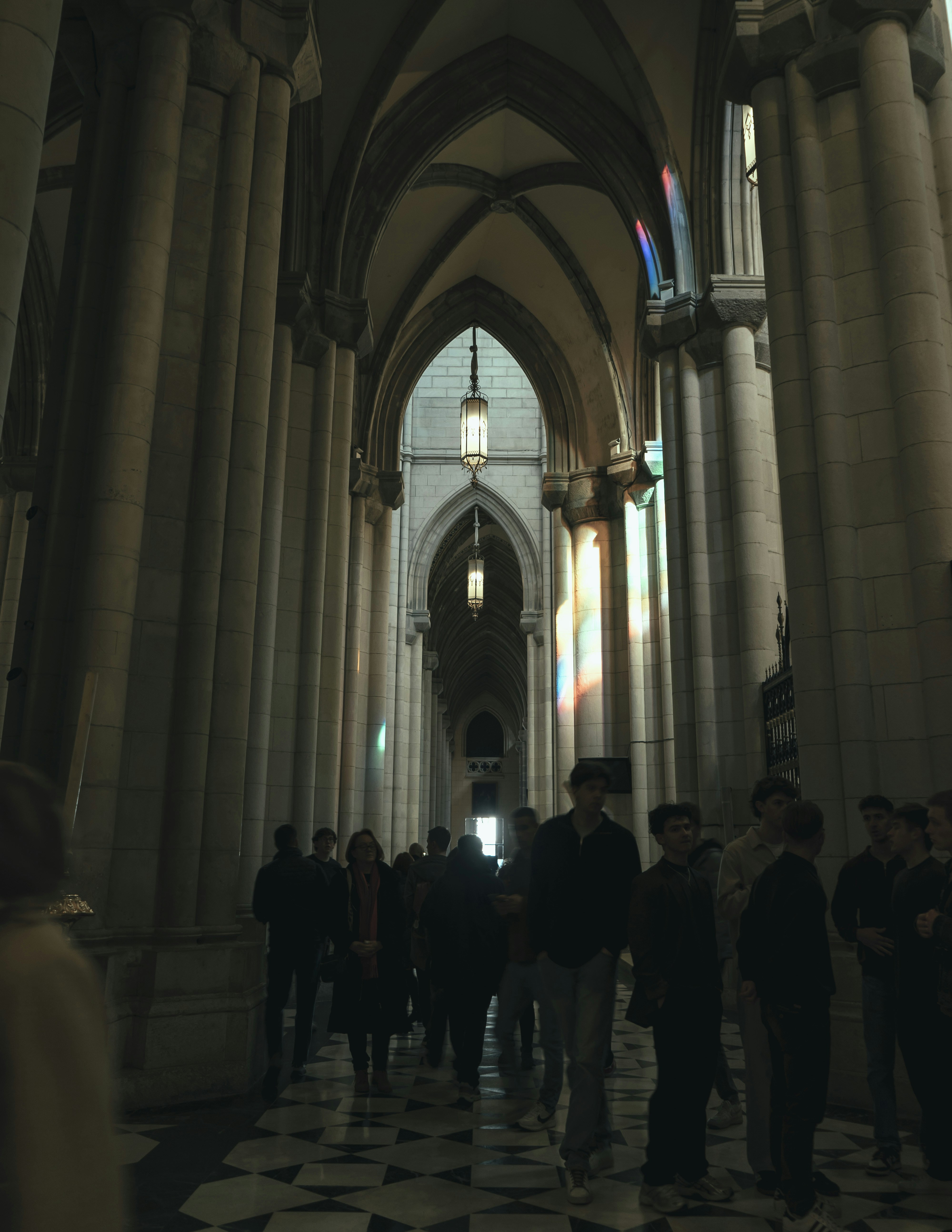 People walk through an arched hallway with sunlight.