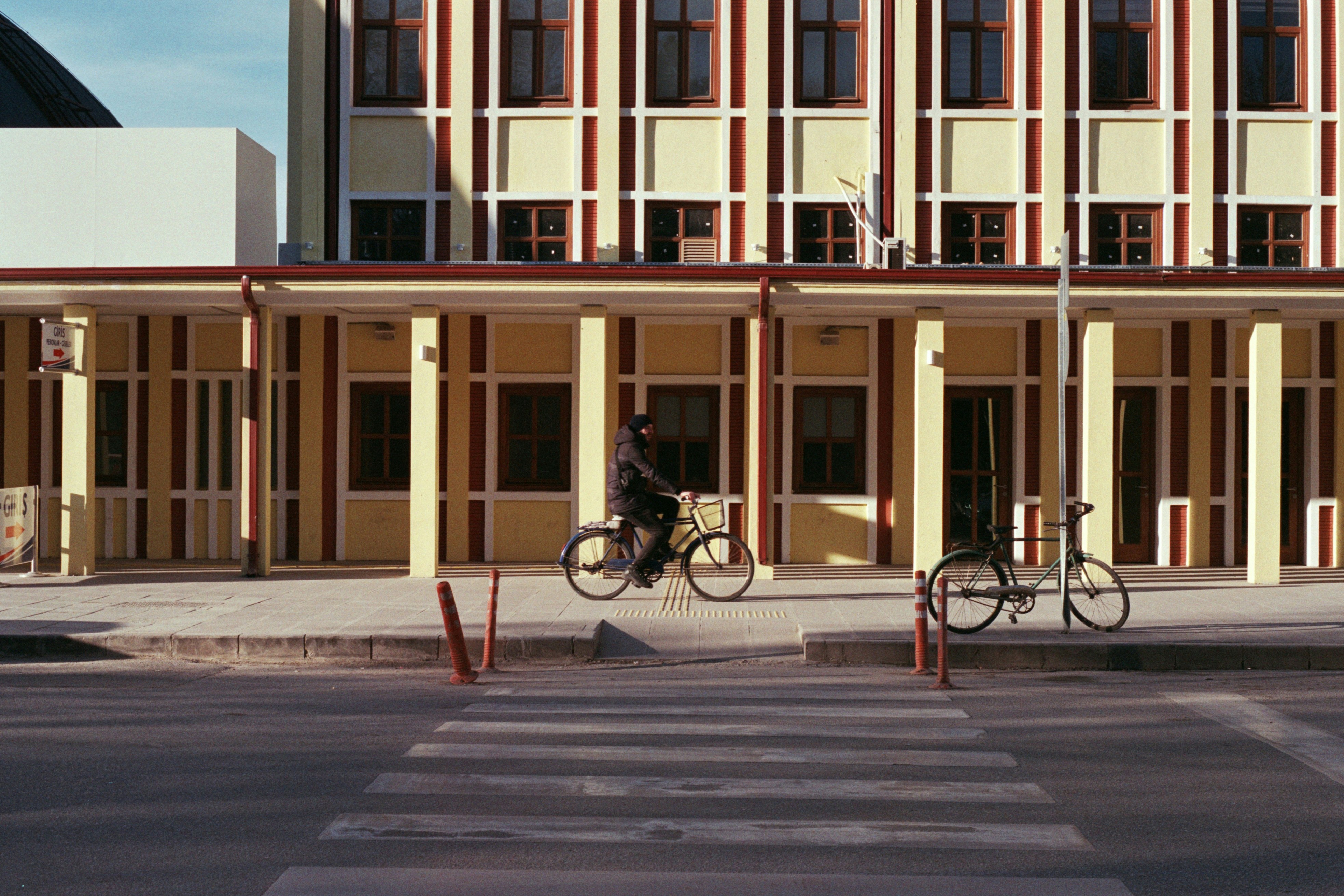 A flat photo of a man riding a bike in front of eskişehir train station. Photo was shot on film (Lomography 100)