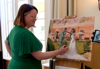 A woman paints a wedding scene on canvas.