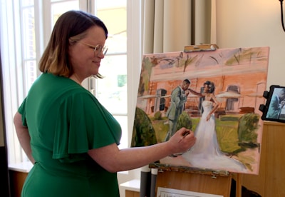 A woman paints a wedding scene on canvas.