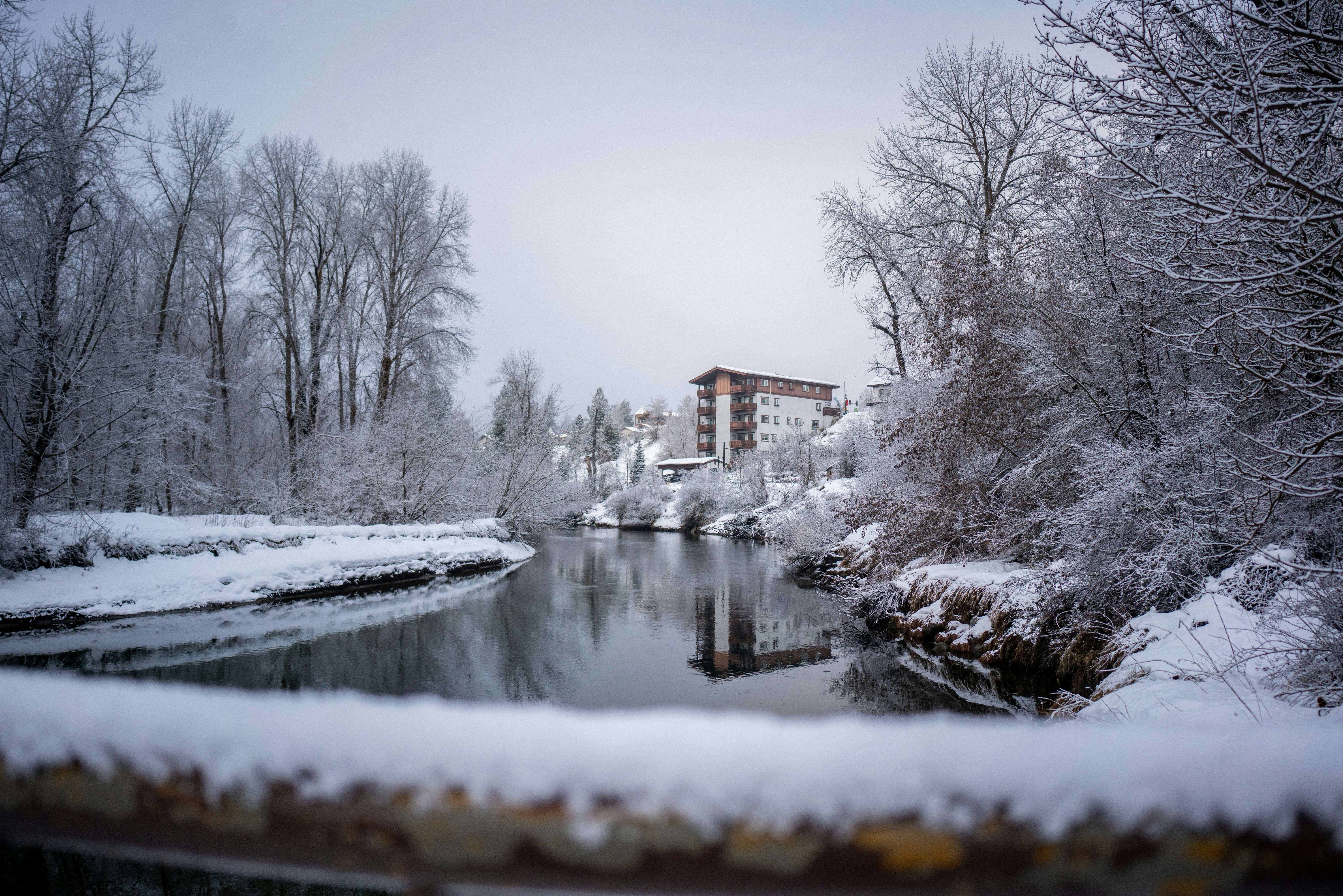 Snowy river landscape with a building in the background.