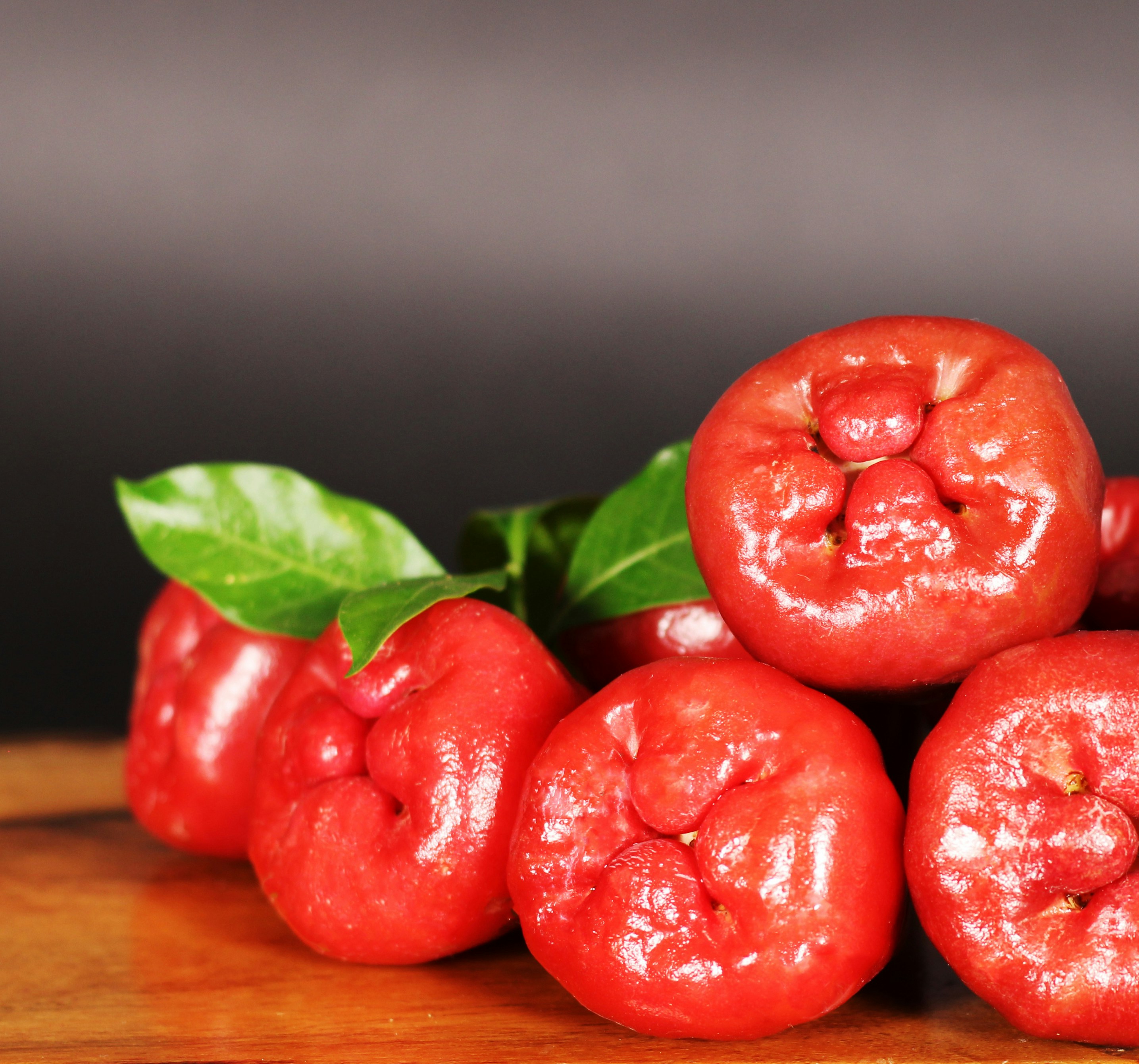A vibrant cluster of ripe rose apples, freshly picked and displayed on a rustic wooden surface. Their glossy red skin and lush green leaves capture the essence of tropical freshness and natural beauty.