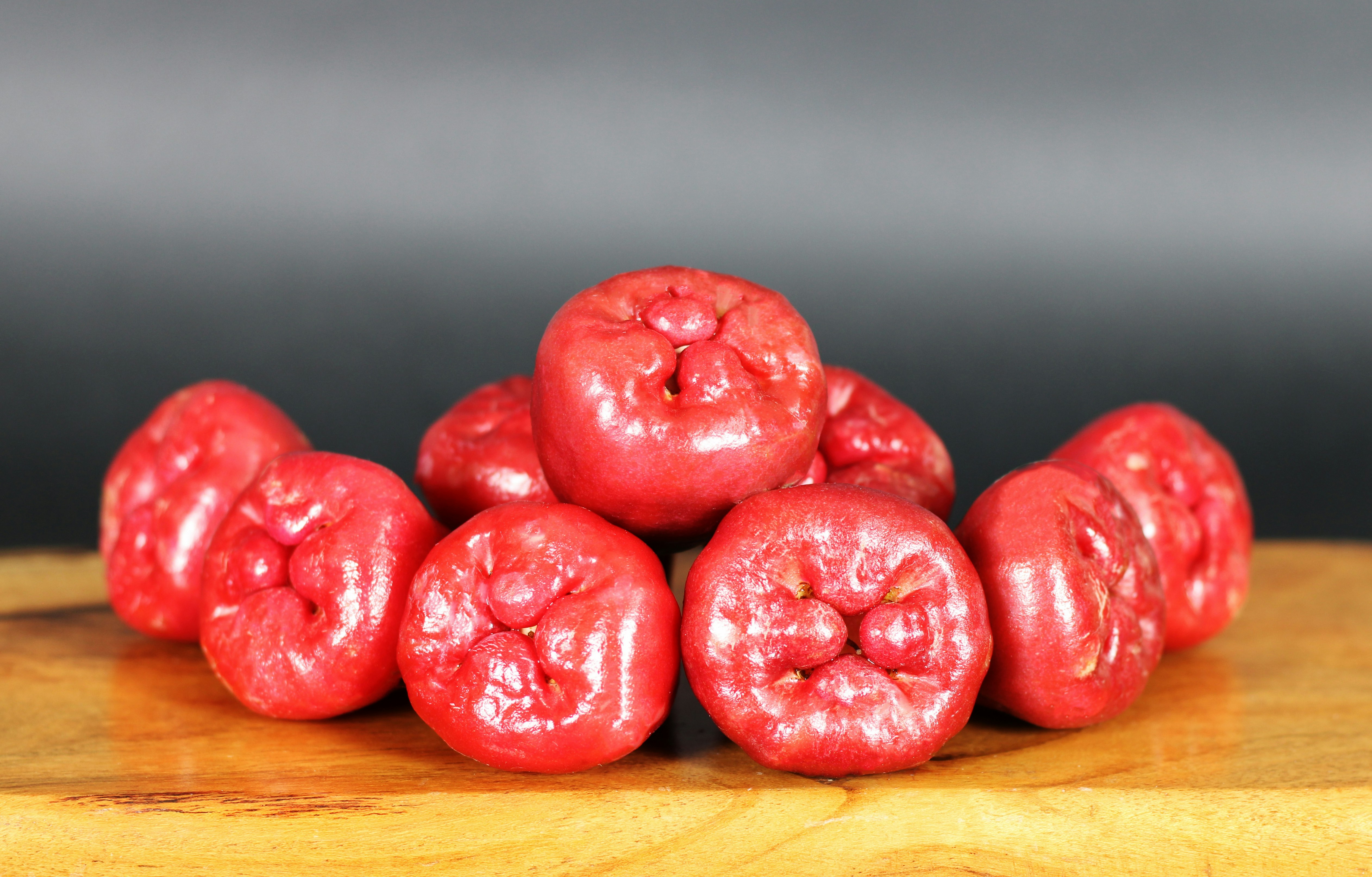 A vibrant cluster of ripe rose apples, freshly picked and displayed on a rustic wooden surface. Their glossy red skin and lush green leaves capture the essence of tropical freshness and natural beauty.