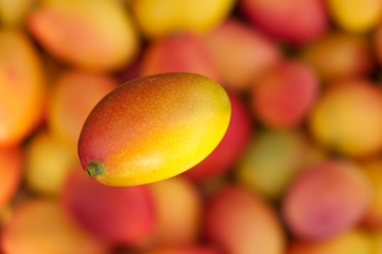 A mango floats above a pile of other mangoes.