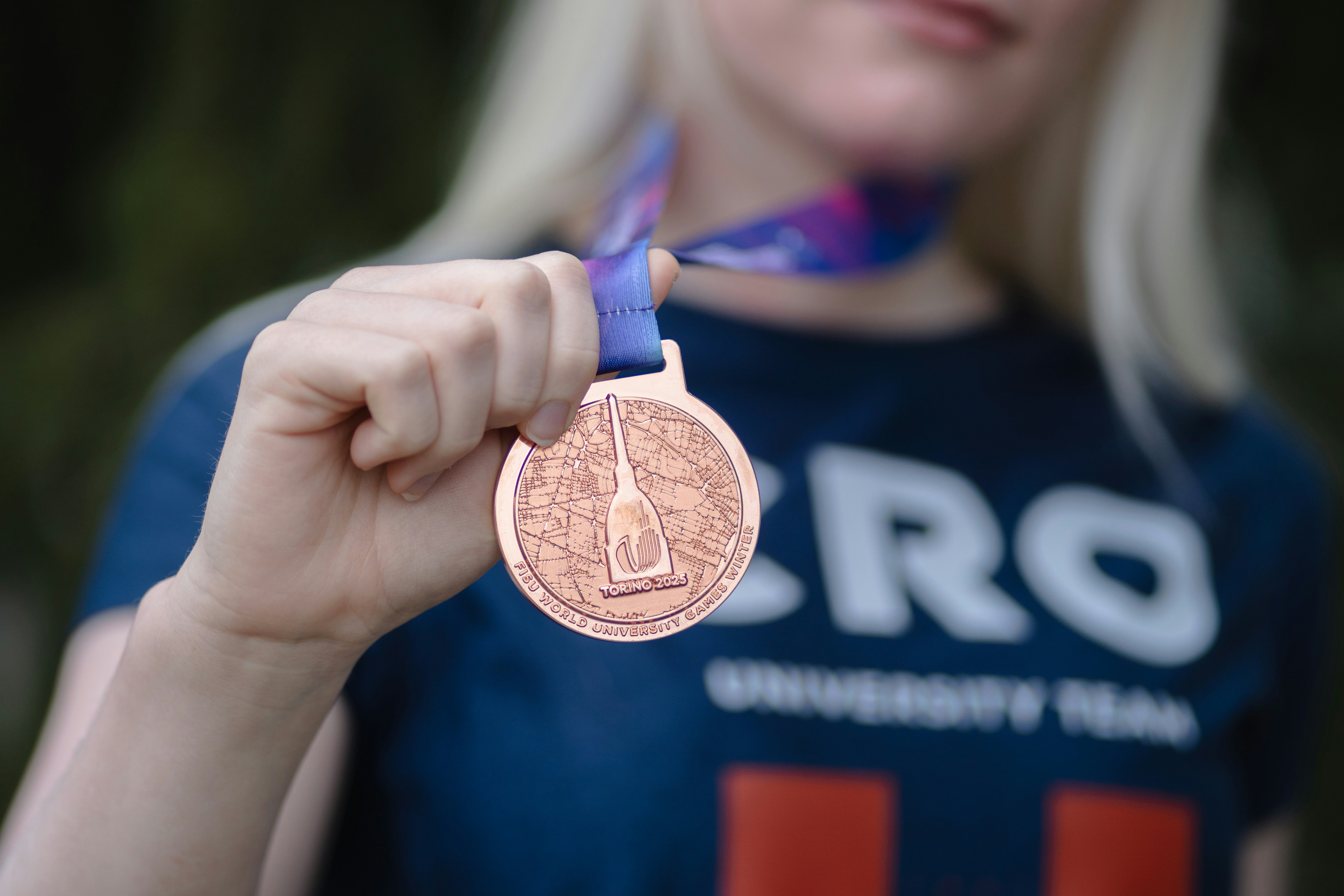 A young woman proudly displays her bronze medal.