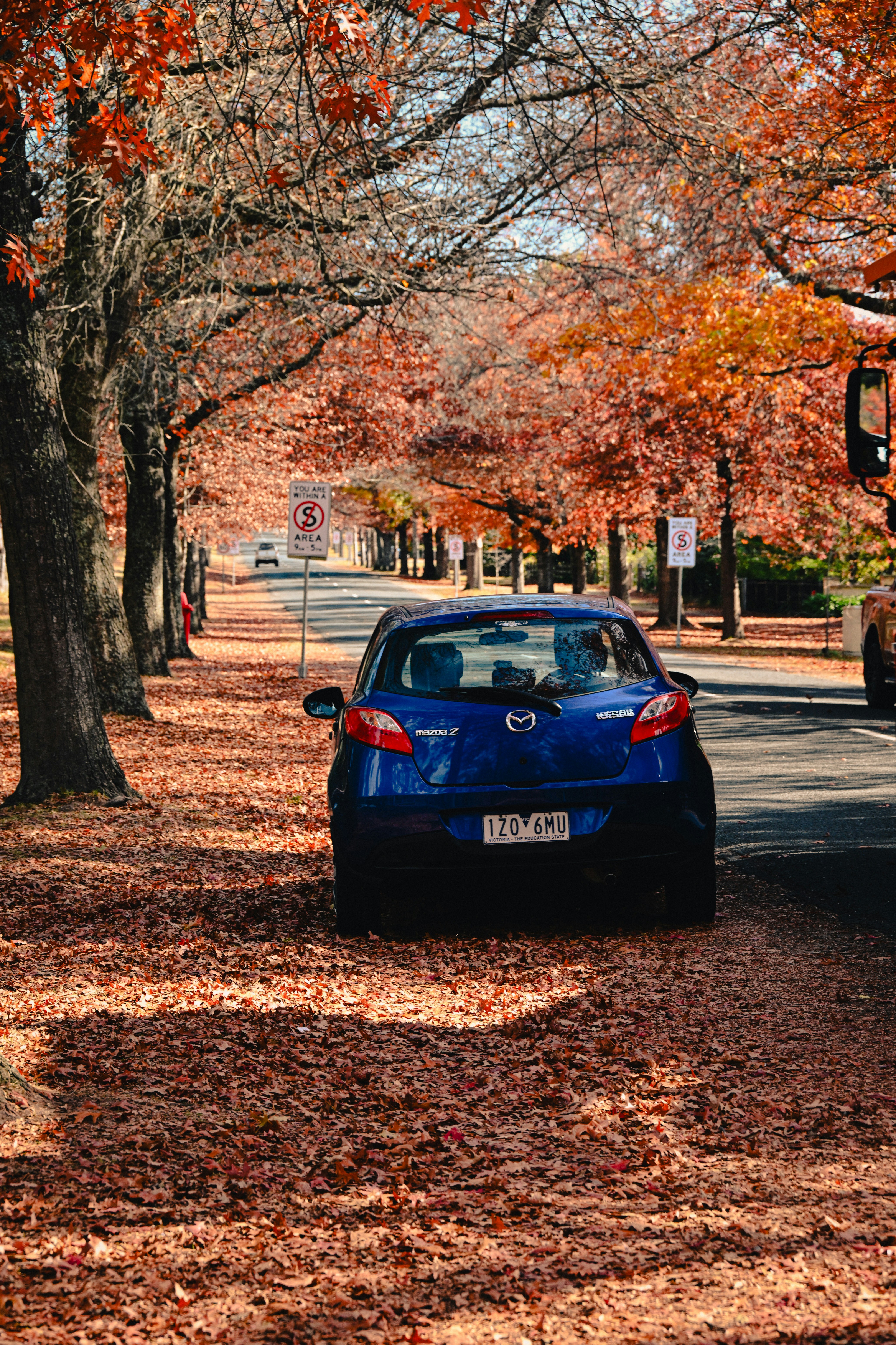 Um carro azul está estacionado sob as árvores de outono.